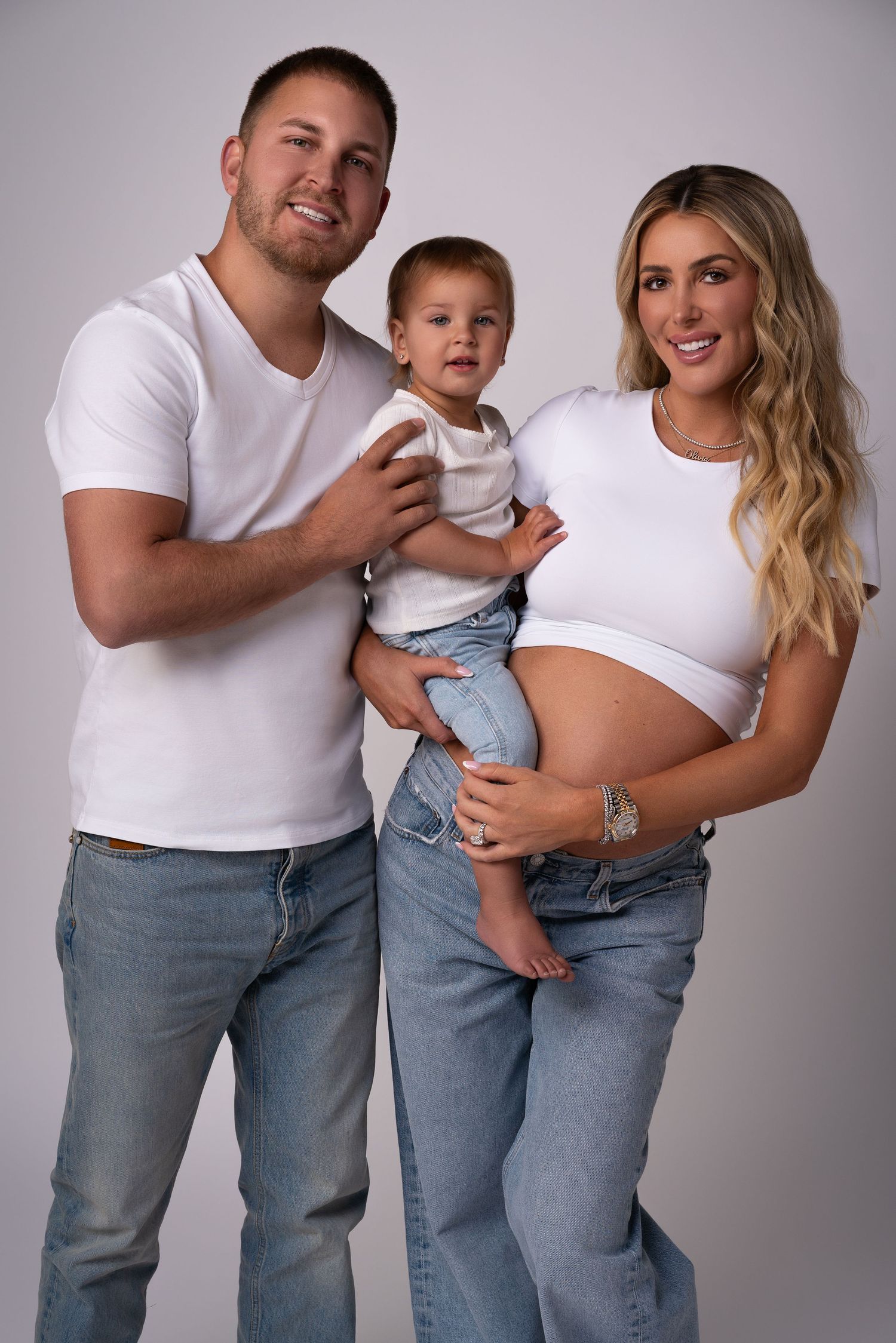 Beautiful young family posing for a maternity photoshoot in Chicago — mom, dad, and daughter wearing matching white shirts and jeans outfits