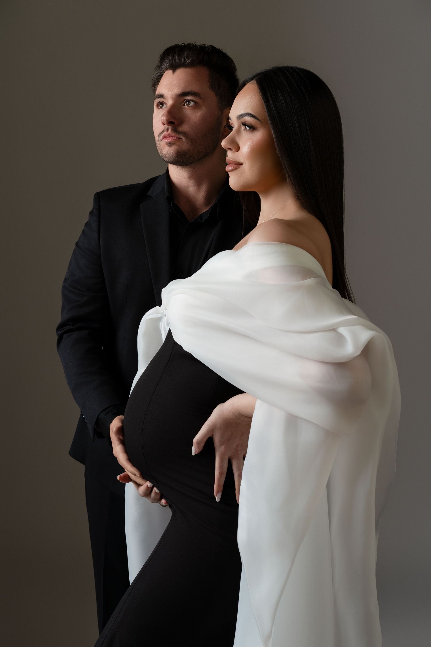 Couple posing face to face during a maternity photoshoot in Chicago; the woman wearing an elegant black dress with white sleeves and the man