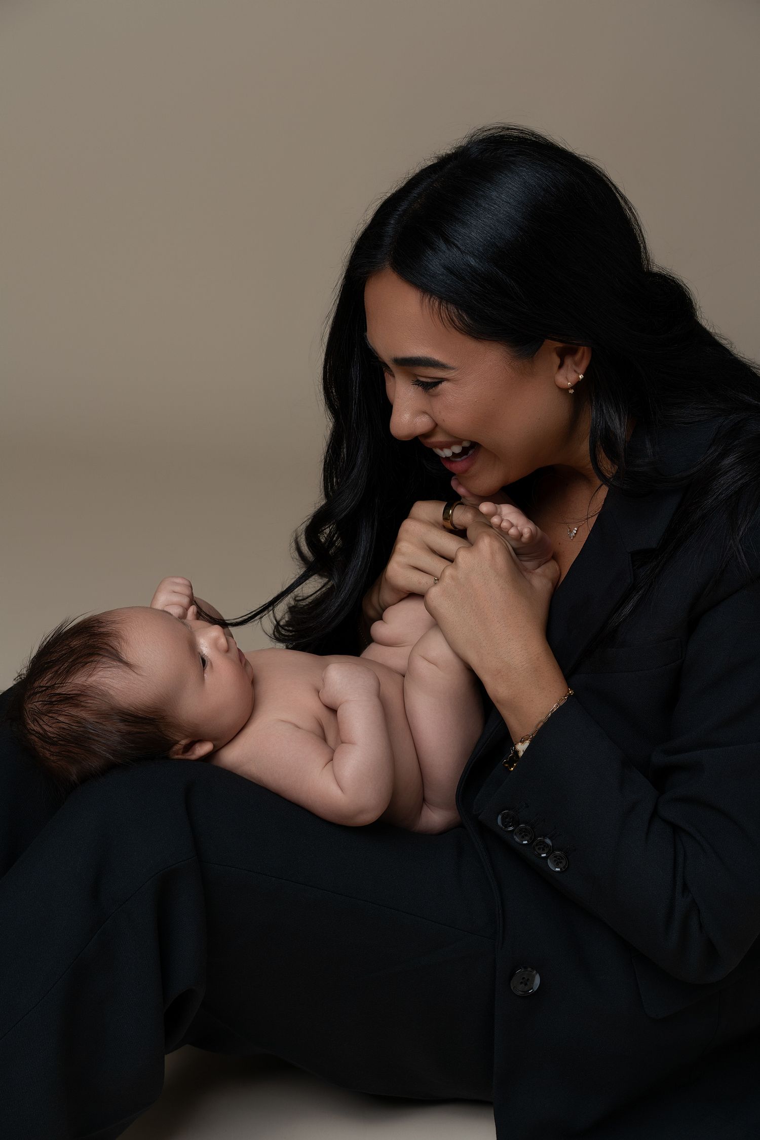 Mommy and Me newborn photoshoot in a Chicago studio, mother wearing a black suit while holding her newborn baby in a tender moment.