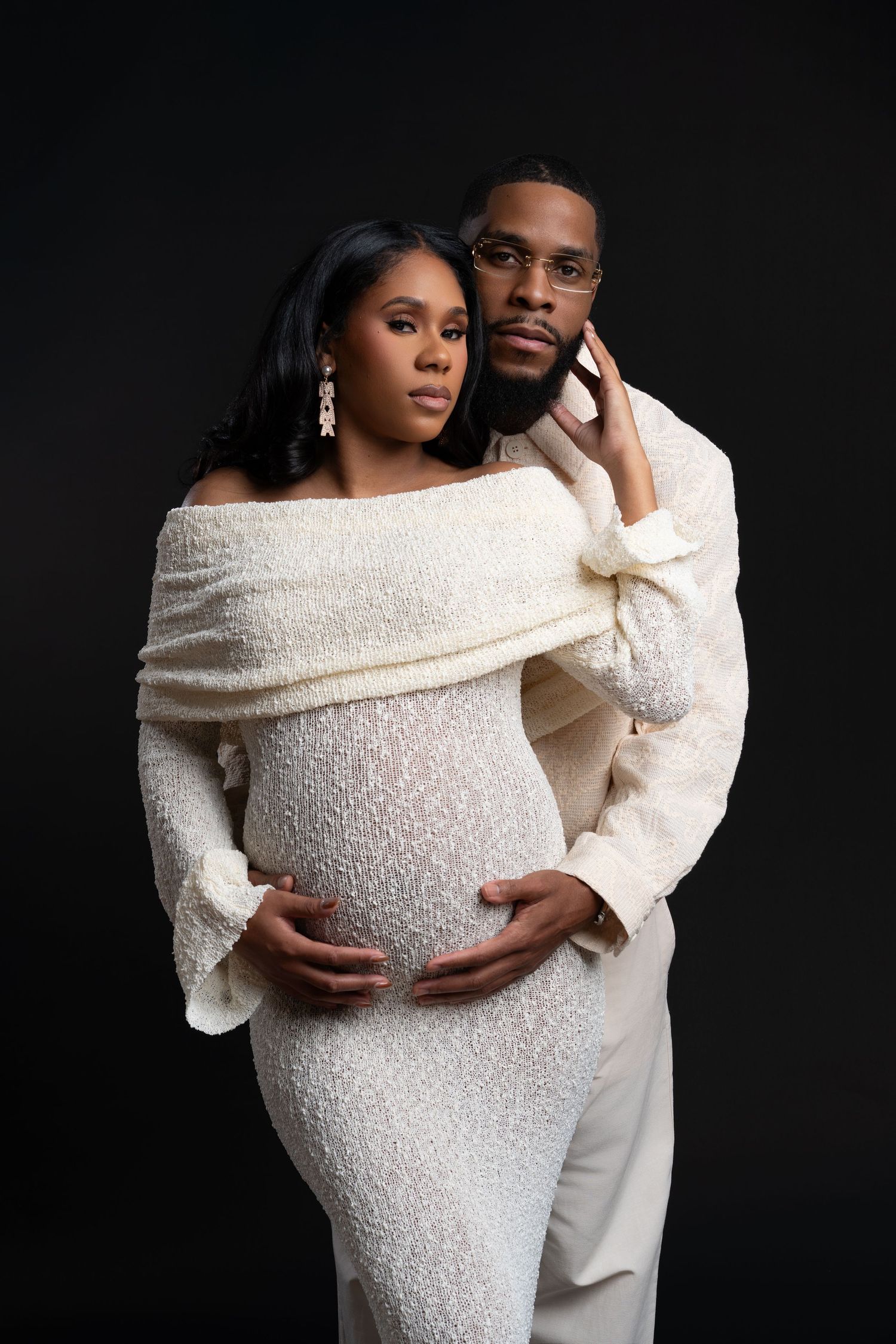 African American couple posing during a maternity photoshoot in the studio in Chicago, wearing white outfits.