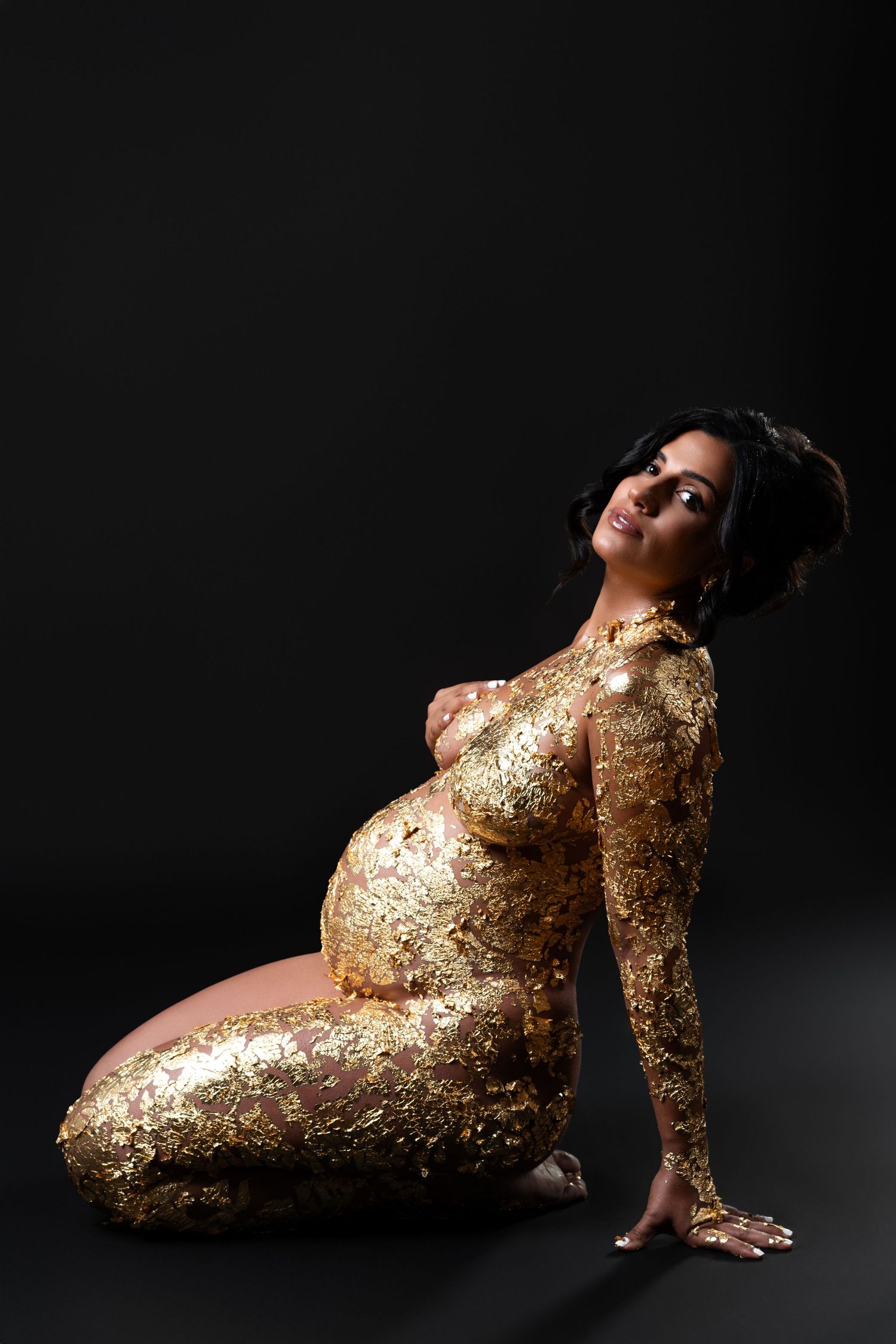 Elegant nude maternity photoshoot for a pregnant woman with golden accents in a Chicago studio.