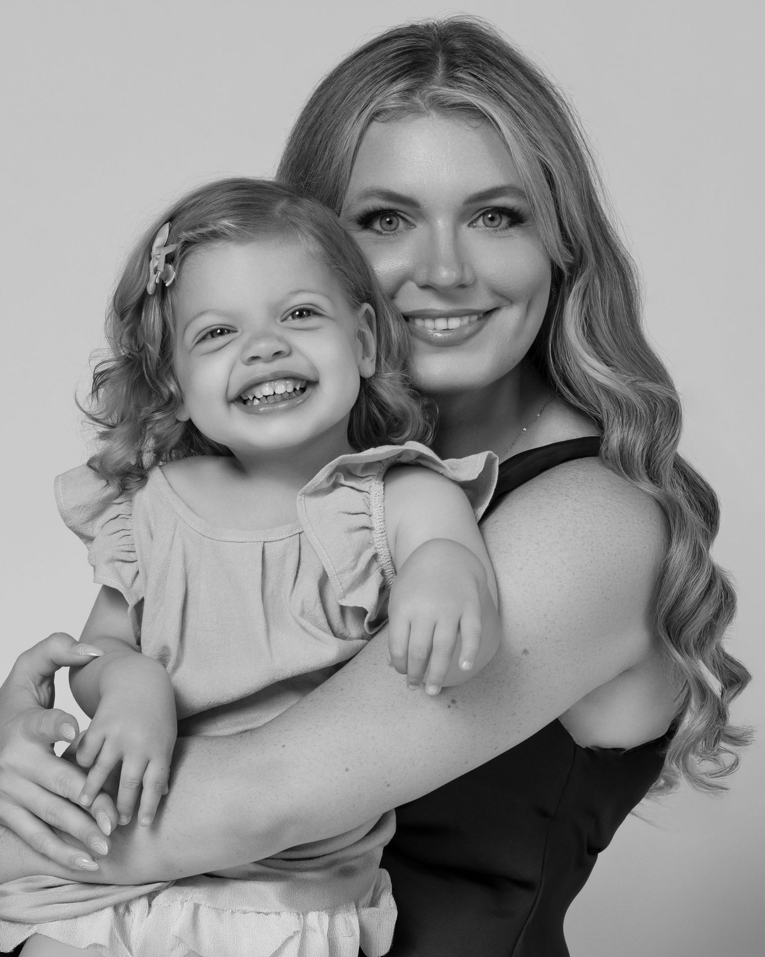 Mommy and daughter portrait session in dresses in a Chicago studio — blonde mother and blonde little 2 years girl. They are smiling.