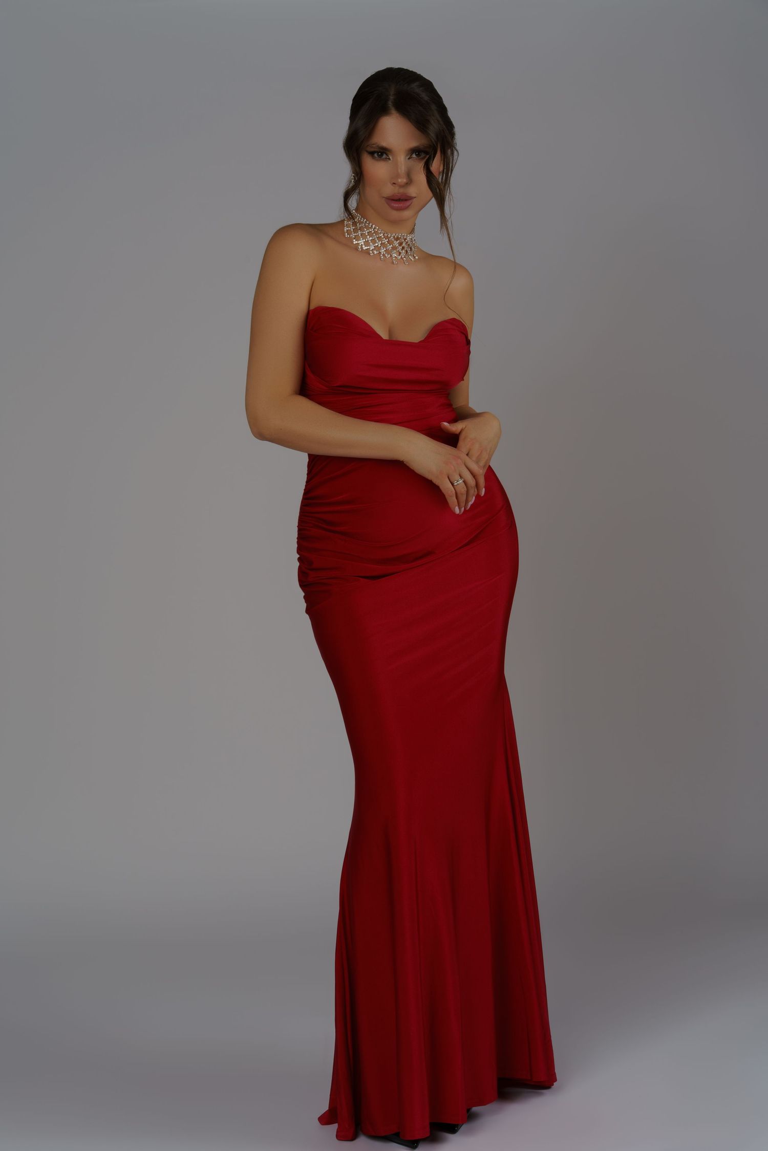 Glamorous brunette in a red evening gown and statement necklace, with styled hair and makeup, posing in a Chicago studio.