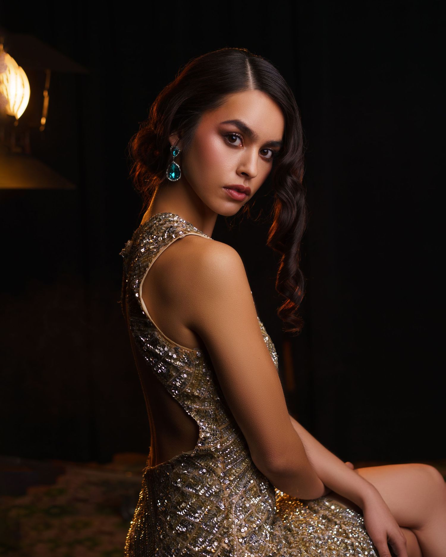 Young woman in a gold dress with blue crystal earrings, evening makeup and hairstyle, posing gracefully — luxury studio portrait in Chicago.
