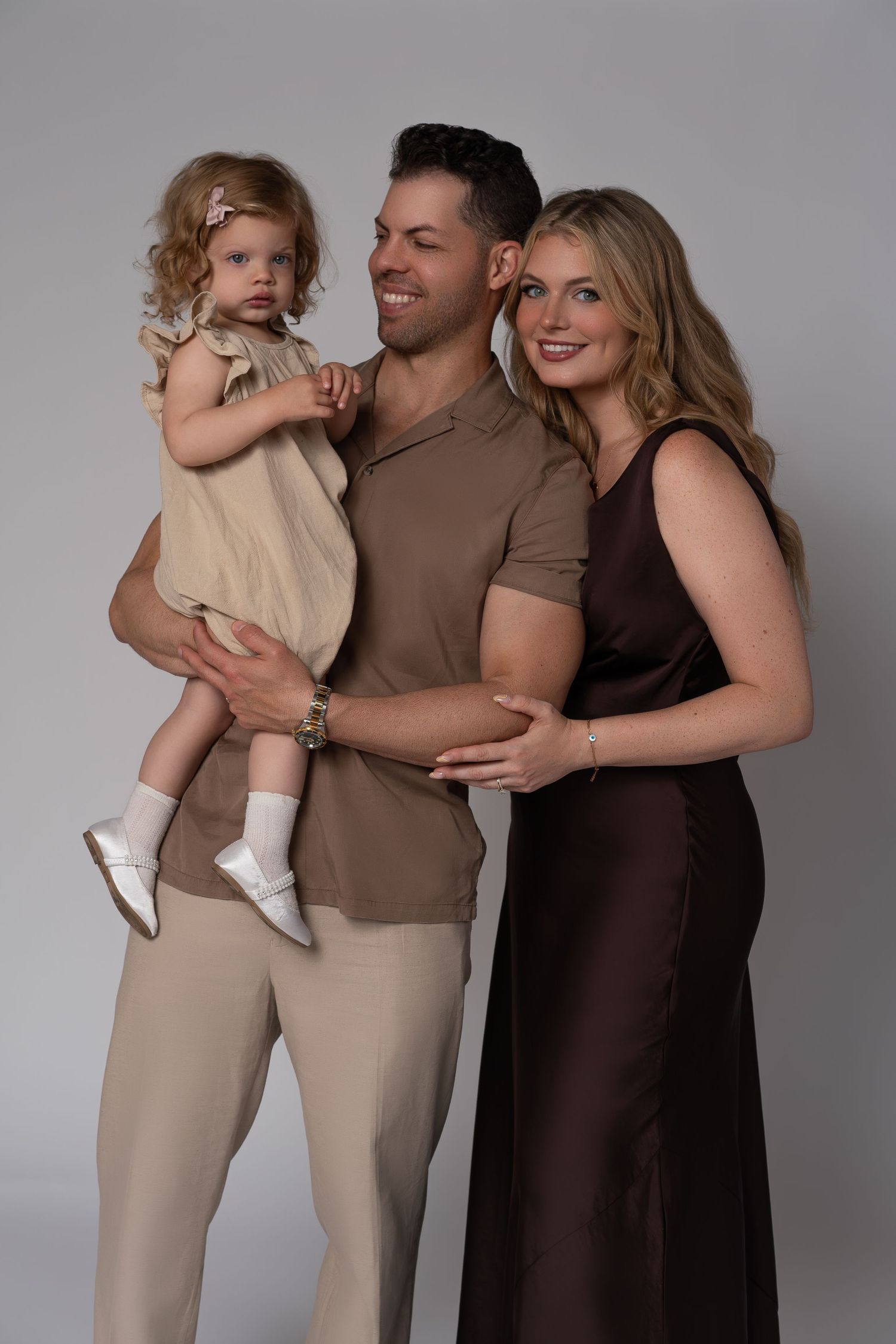 Young family during a family photoshoot in Chicago, posing in beige and brown outfits with their 3-year-old daughter.