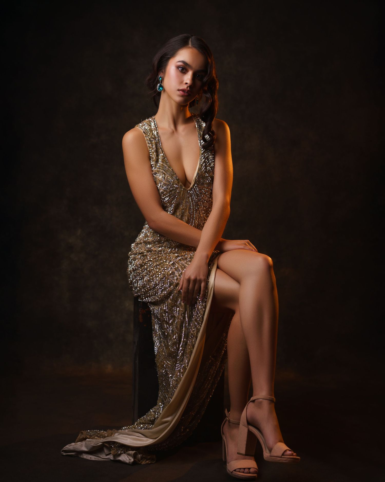 Young woman in a gold dress with blue crystal earrings, evening makeup and hairstyle, posing gracefully — luxury studio portrait in Chicago.