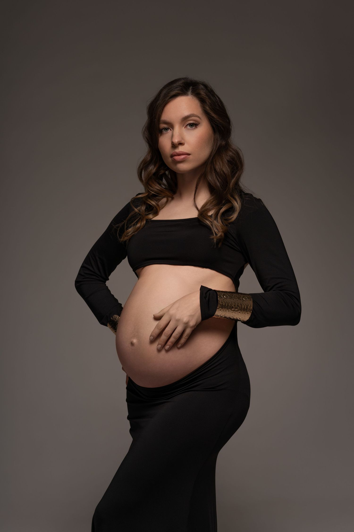 Maternity portrait of a stylish expecting mother posing in long black dress with confidence and grace in Chicago studio.