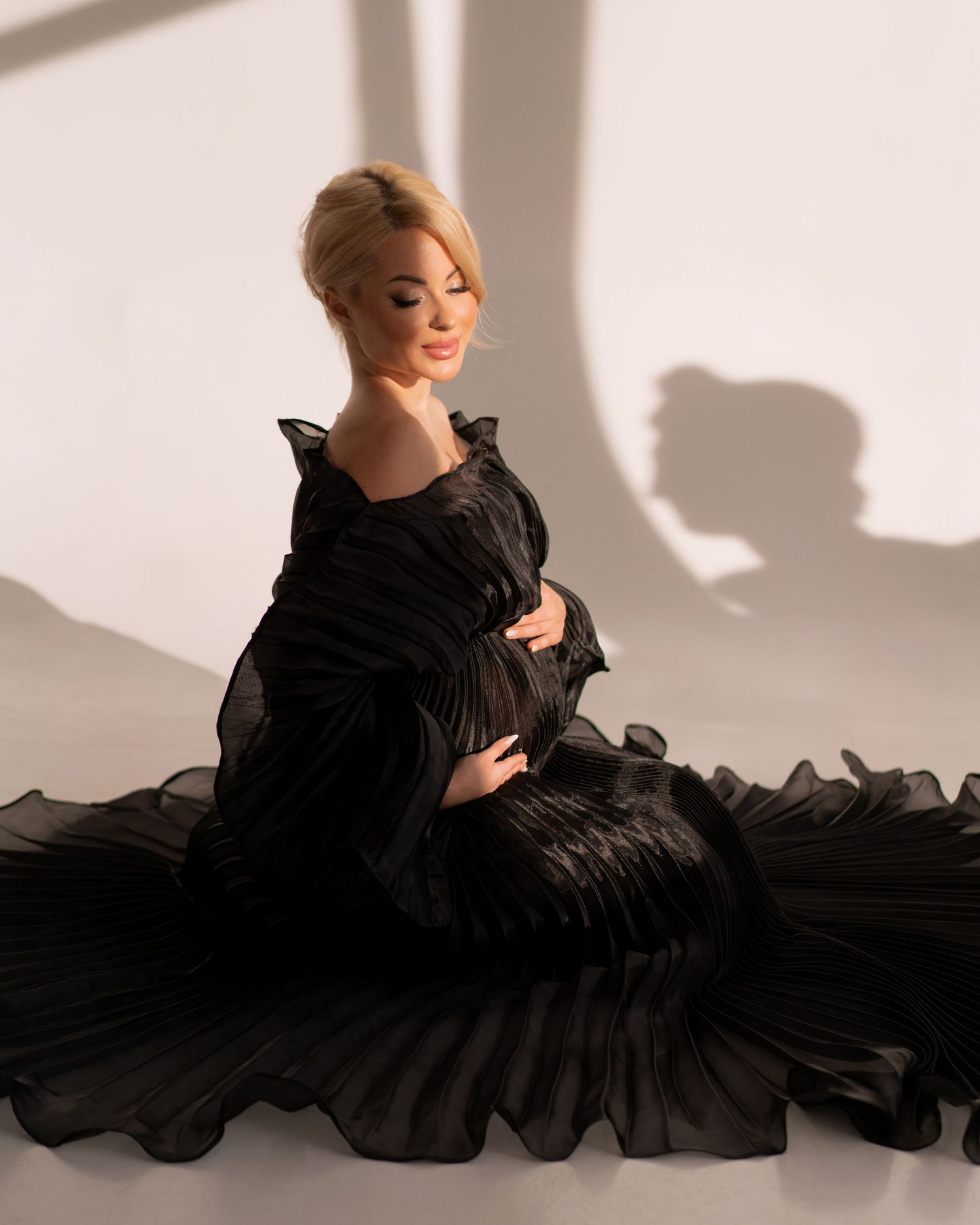 Pregnant women posing in black luxury gown holding hands over the baby bump.