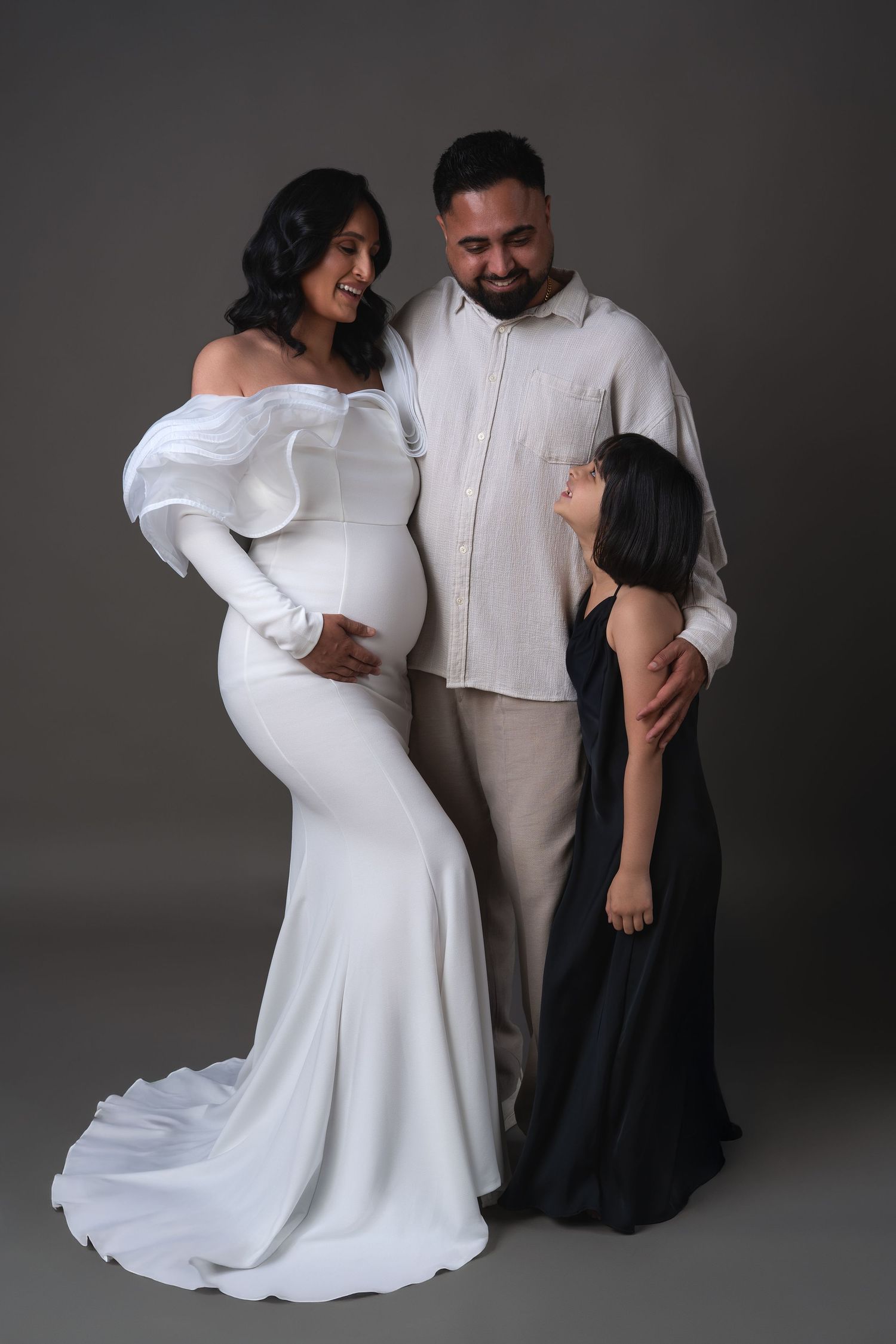 Maternity family photoshoot — pregnant woman in long white dress with her husband and daughter posing during maternity shoot in Chicago.