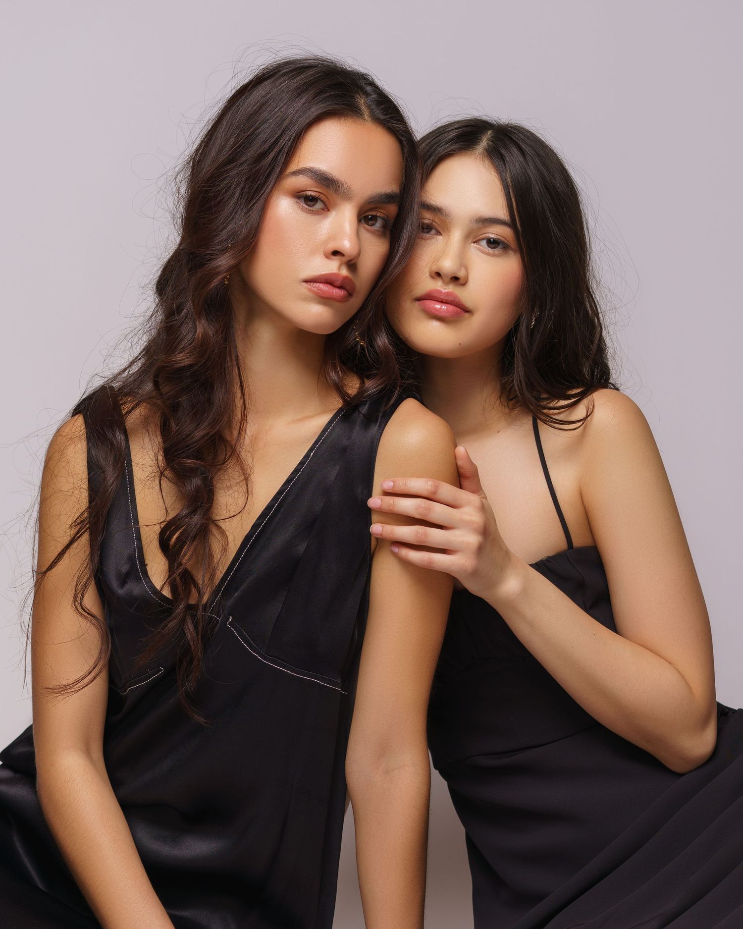 Two beautiful young sisters in matching black silk dresses posing for an elegant family photoshoot in a Chicago studio.