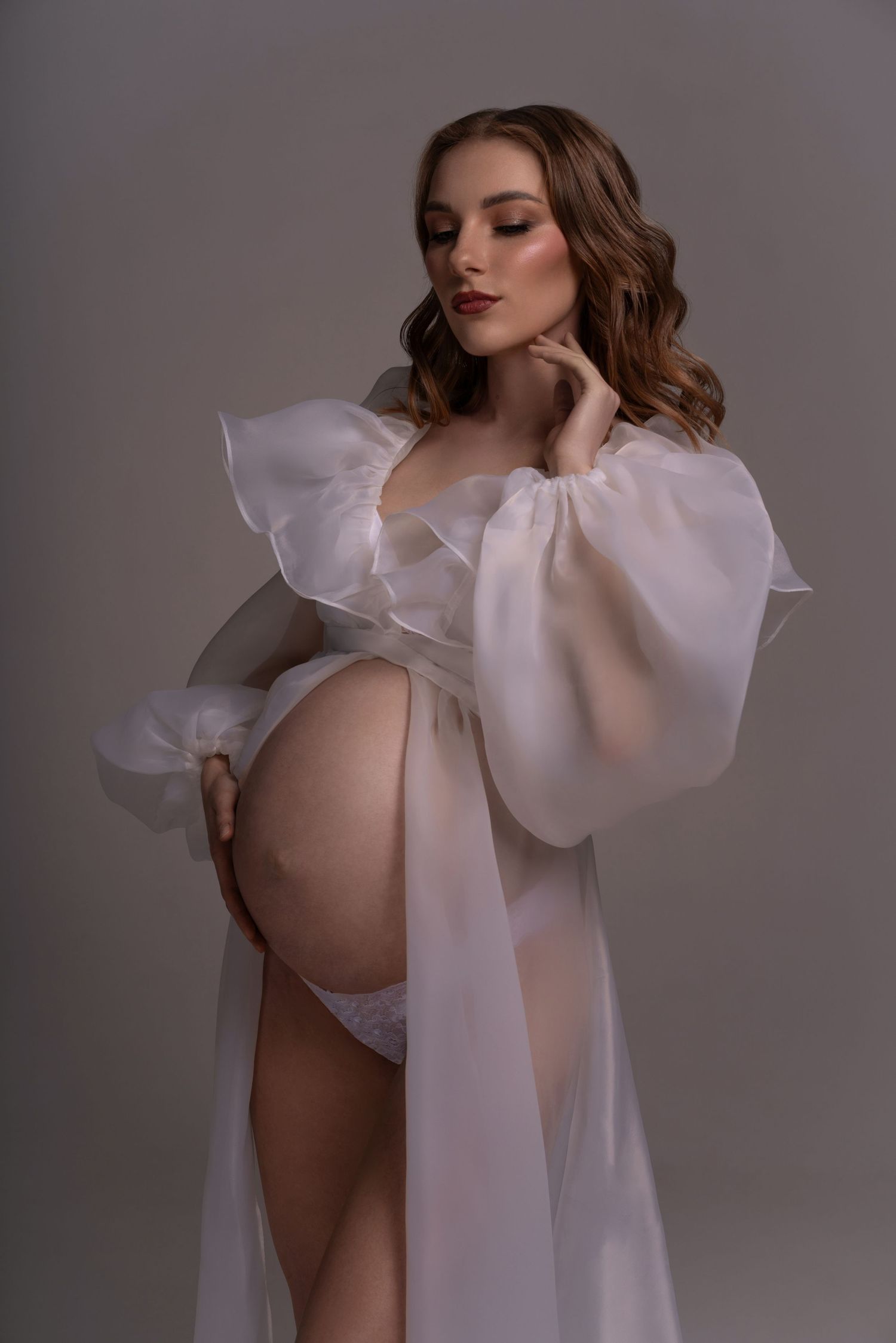 The pregnant women posing in white couture gown holding her hands on belly bump during maternity photoshoot in Chicago.