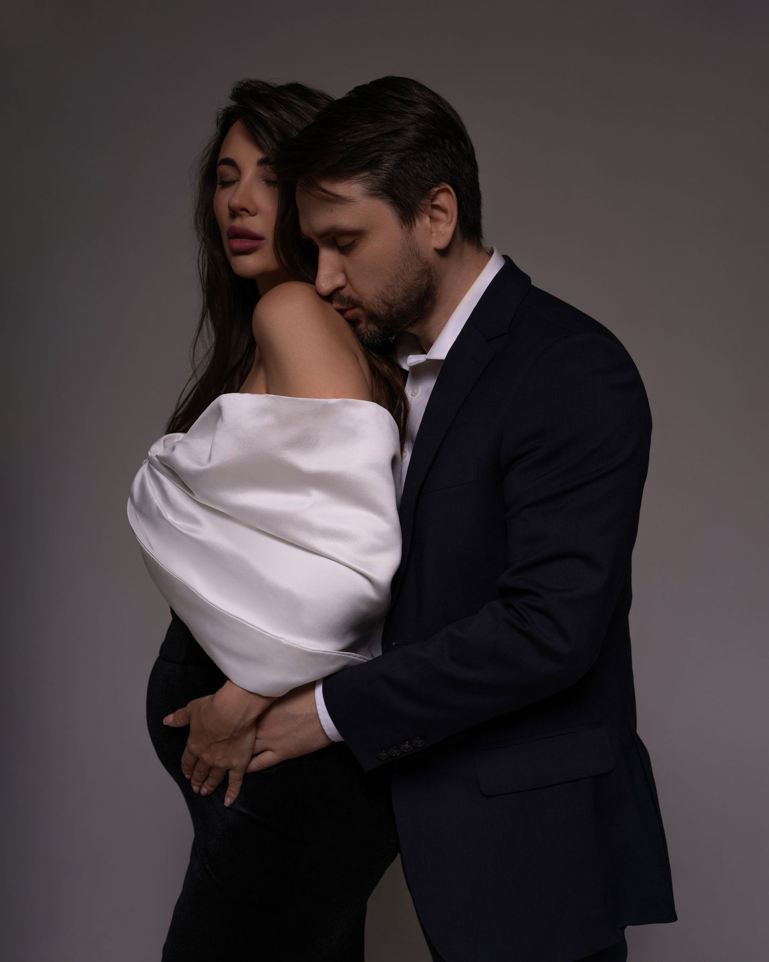 Artistic maternity photo showcasing the deep bond between expecting parents, the dad is kissing of women's shoulder.