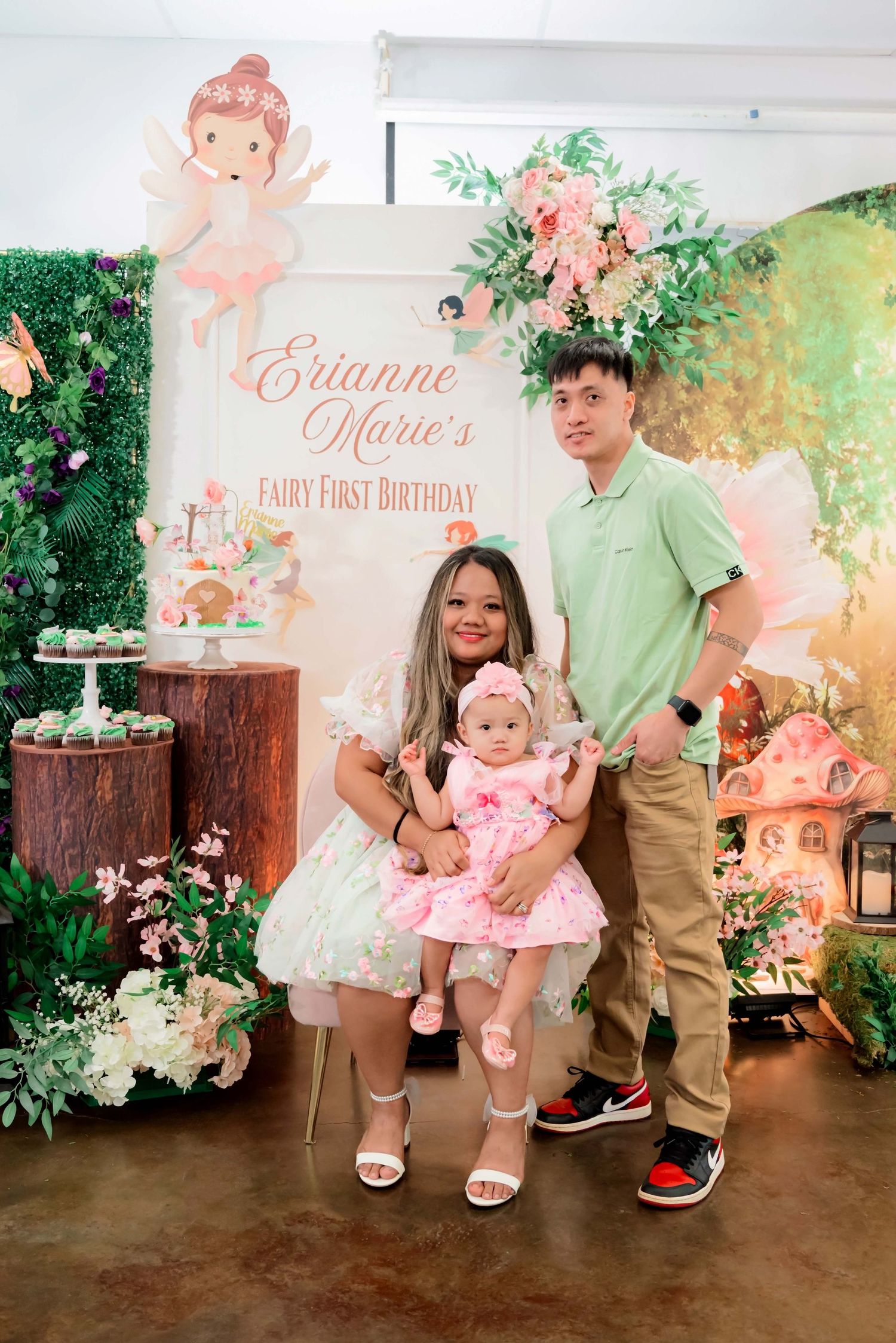 Family posing at Erianne Marie's Fairy First Birthday party with floral backdrop and fairy tale decorations.