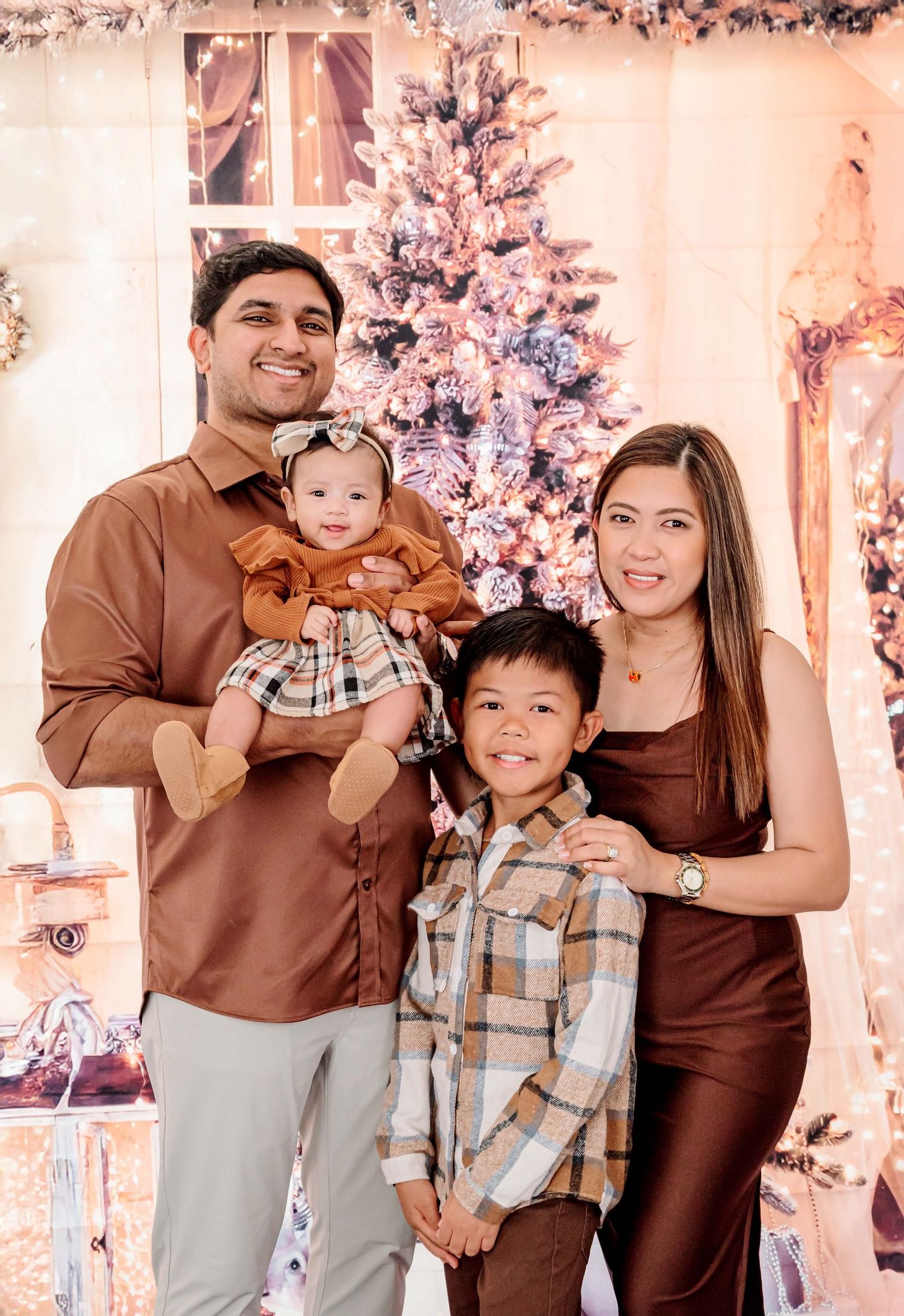 Family of four posing in front of a decorated Christmas tree, wearing coordinated brown outfits for a festive holiday photo.