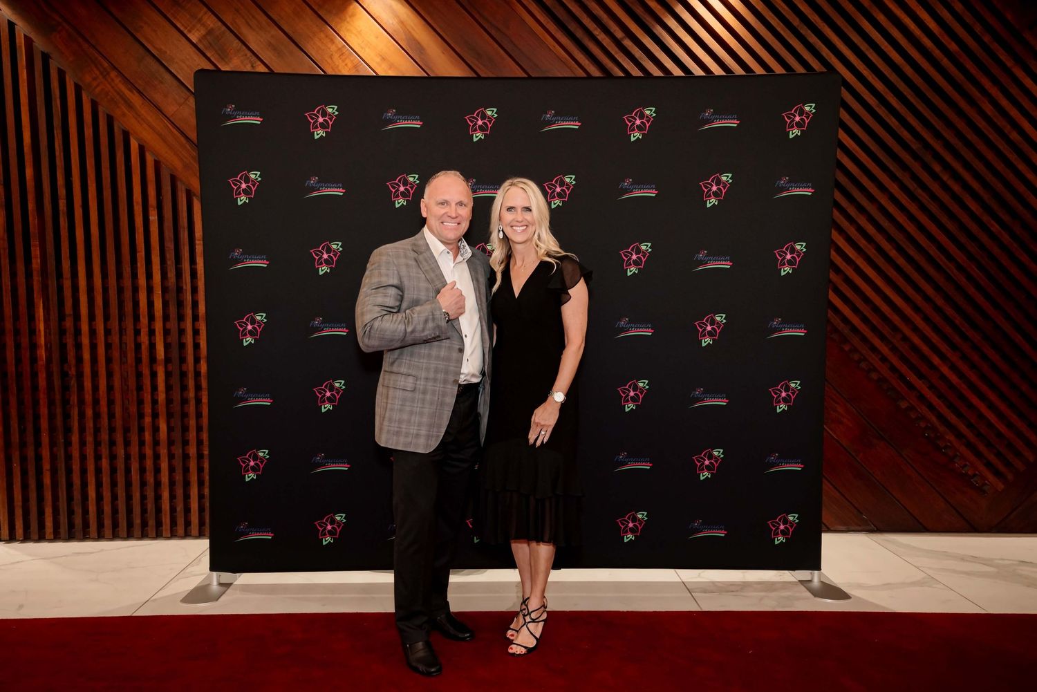 Man and woman posing together on red carpet at formal event in front of branded step-and-repeat backdrop.