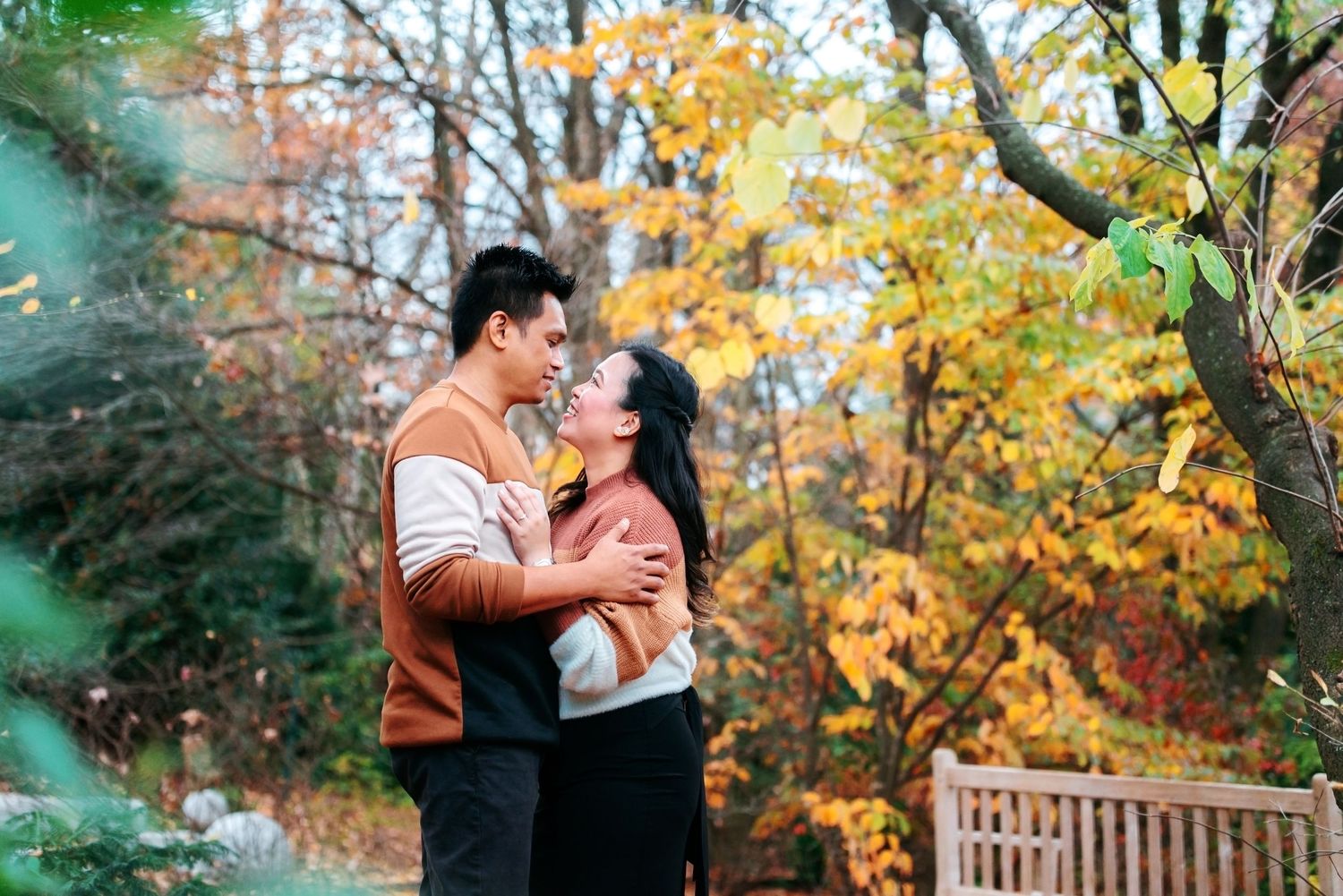 Couple embracing romantically in a colorful autumn park with vibrant orange and yellow foliage in the background.