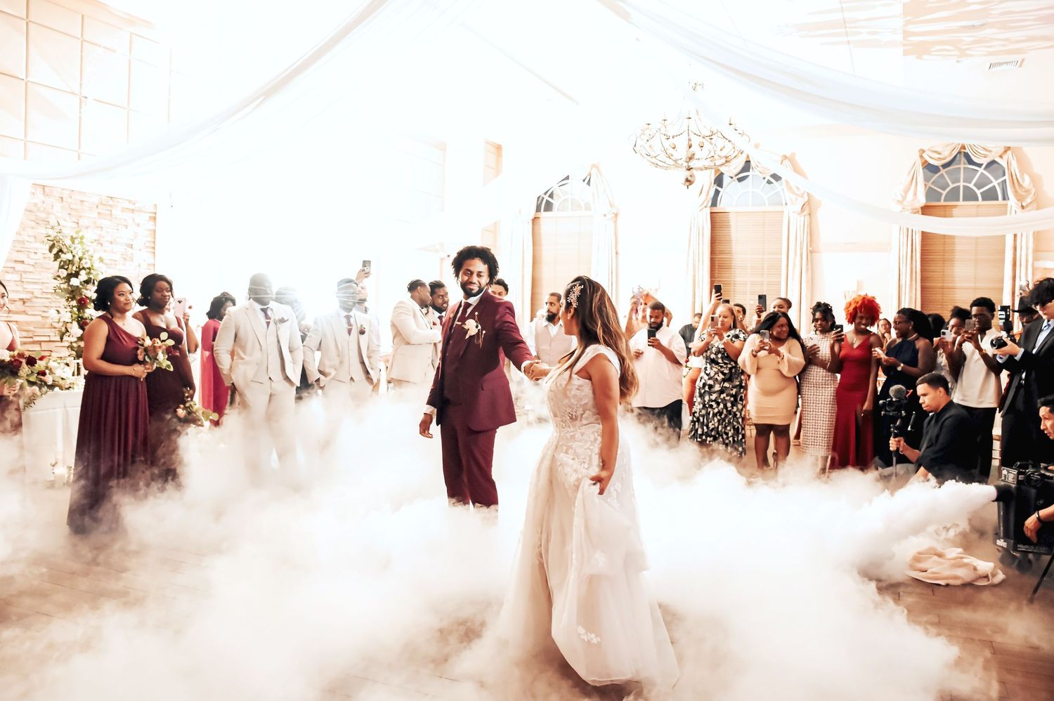 Bride and groom share first dance surrounded by dramatic fog machine smoke at elegant wedding reception.
