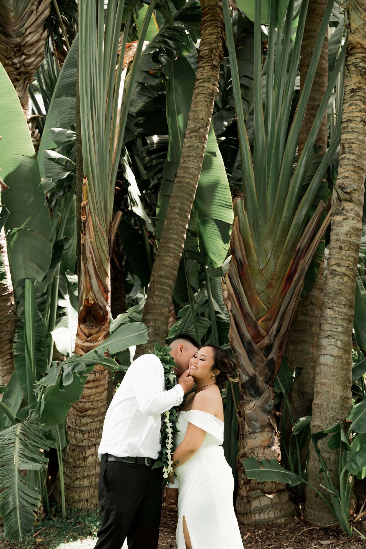 Bride and groom share a romantic moment surrounded by lush tropical palm trees in a stunning outdoor wedding setting.