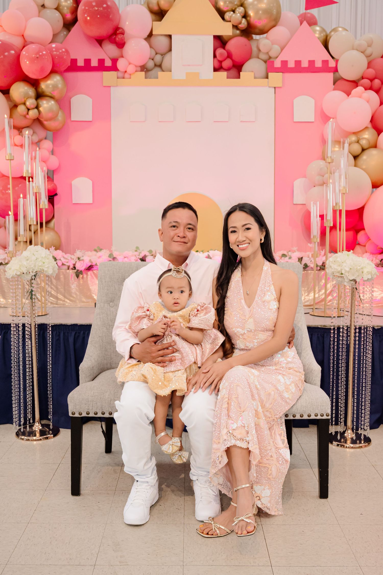 Family posing in front of a pink castle balloon backdrop at a baby girl’s first birthday party celebration.