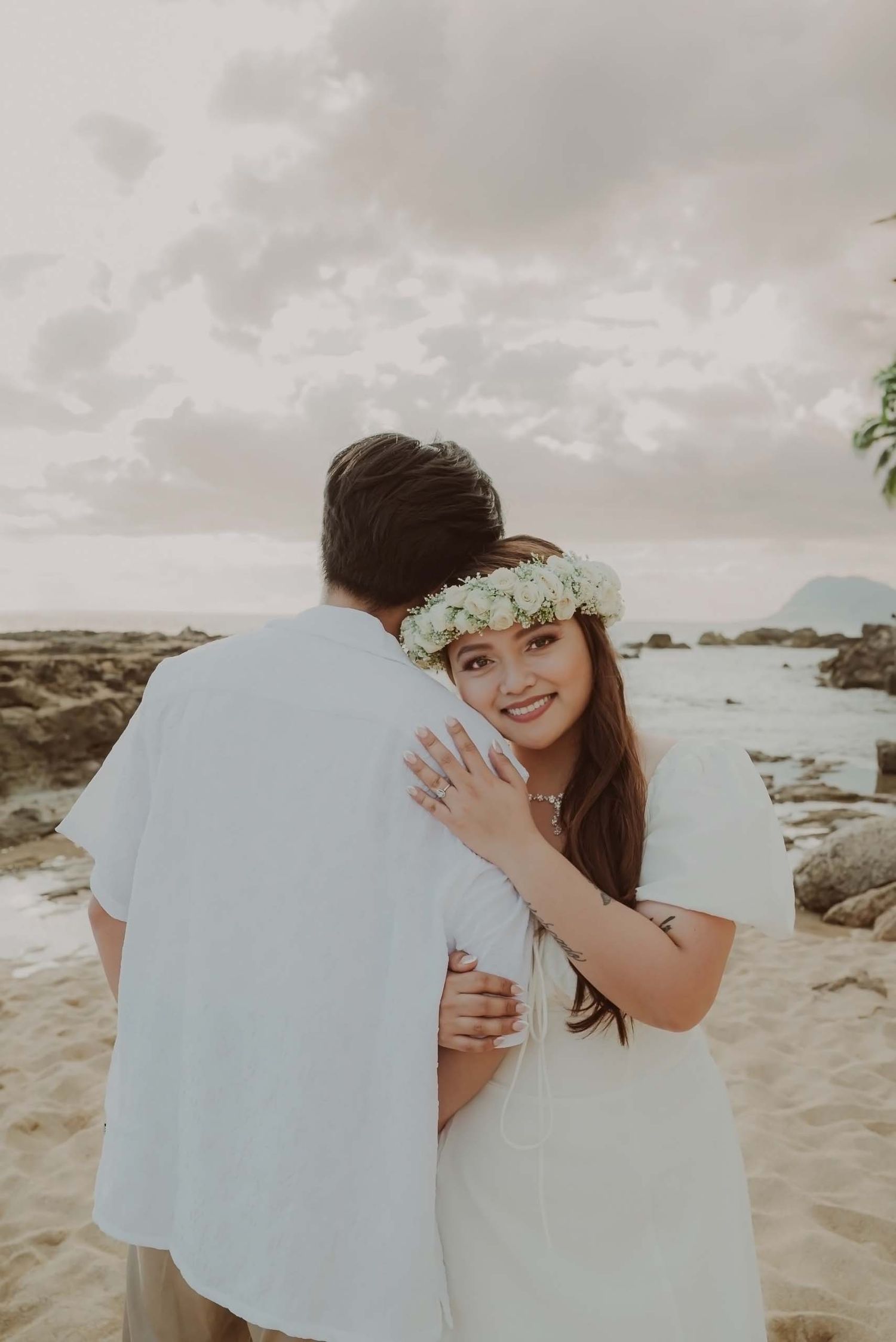 A romantic beach photo series showing a couple in white sharing a tender moment by the ocean at sunset.
