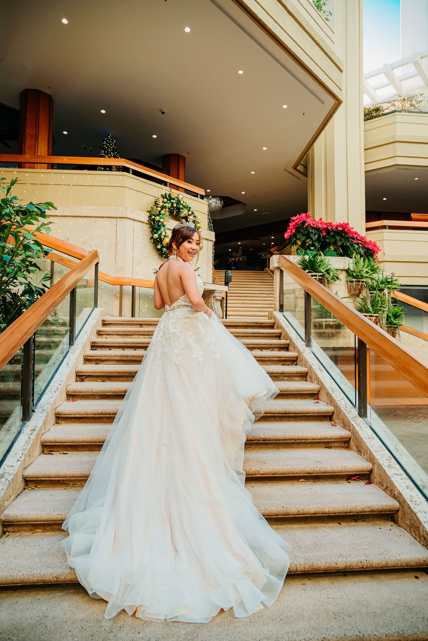 Bride in a flowing white ballgown with lace details poses on elegant staircase at a luxury wedding venue.
