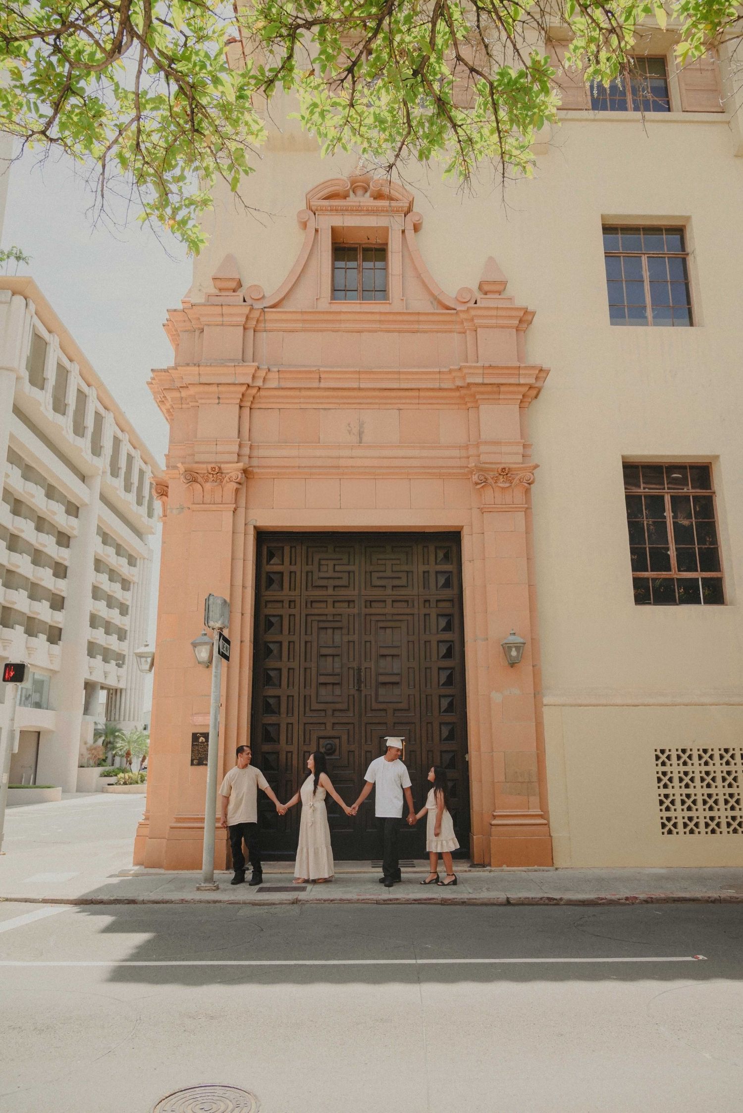 Family of four holding hands in front of an ornate peach-colored building entrance with large wooden doors.
