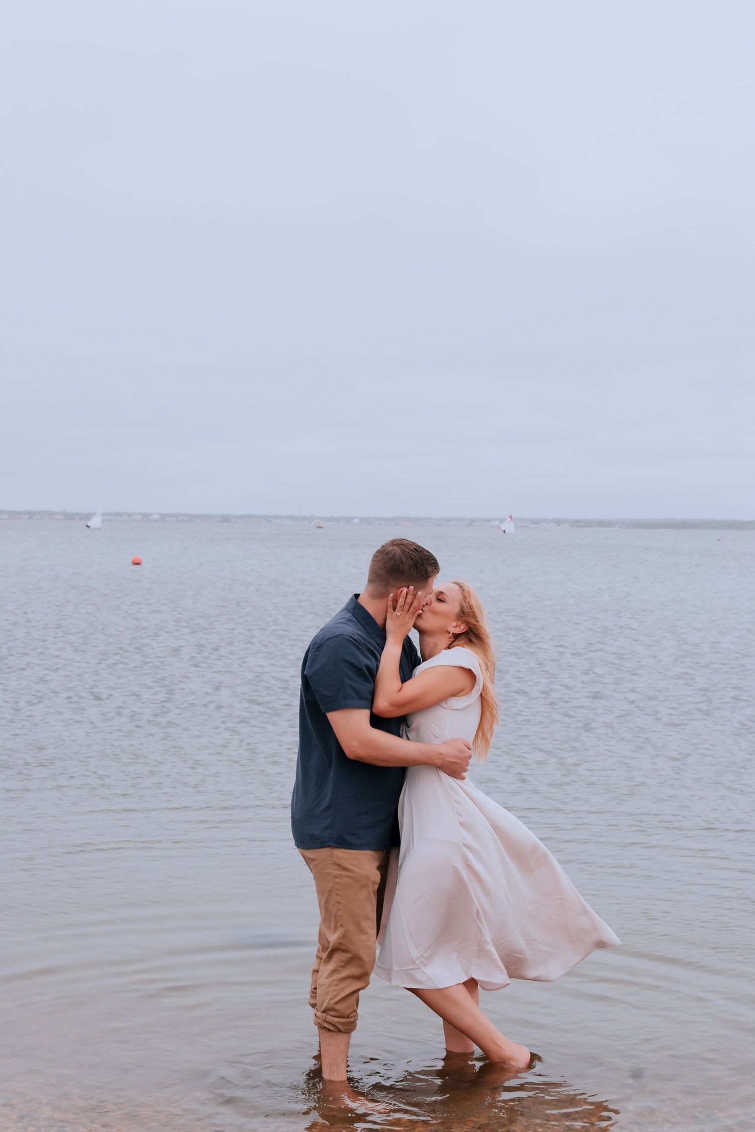 A romantic couple shares a tender moment while standing in shallow ocean waters at sunset.