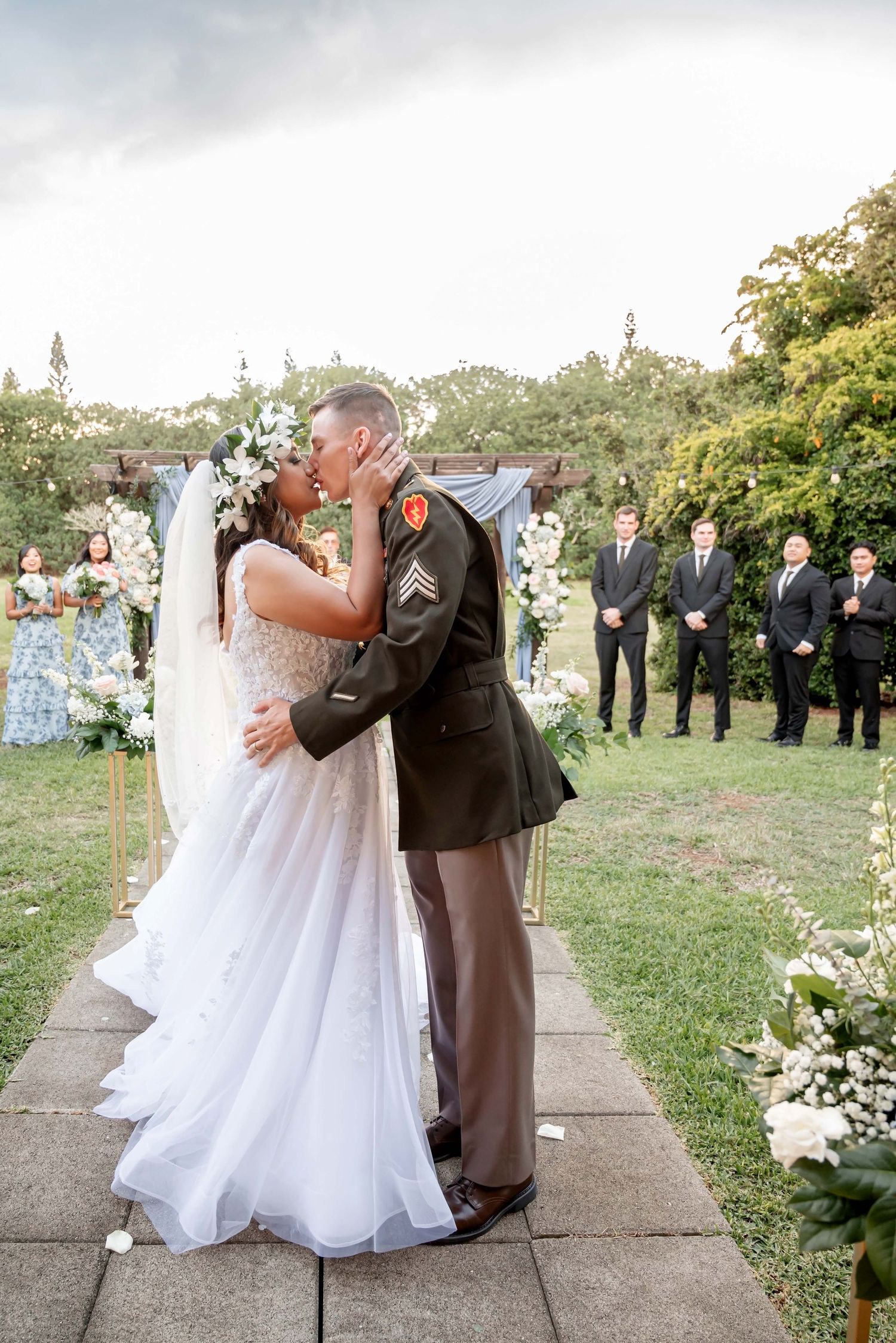Playful wedding couple shares an intimate dipping kiss in a scenic vineyard garden setting during golden hour.