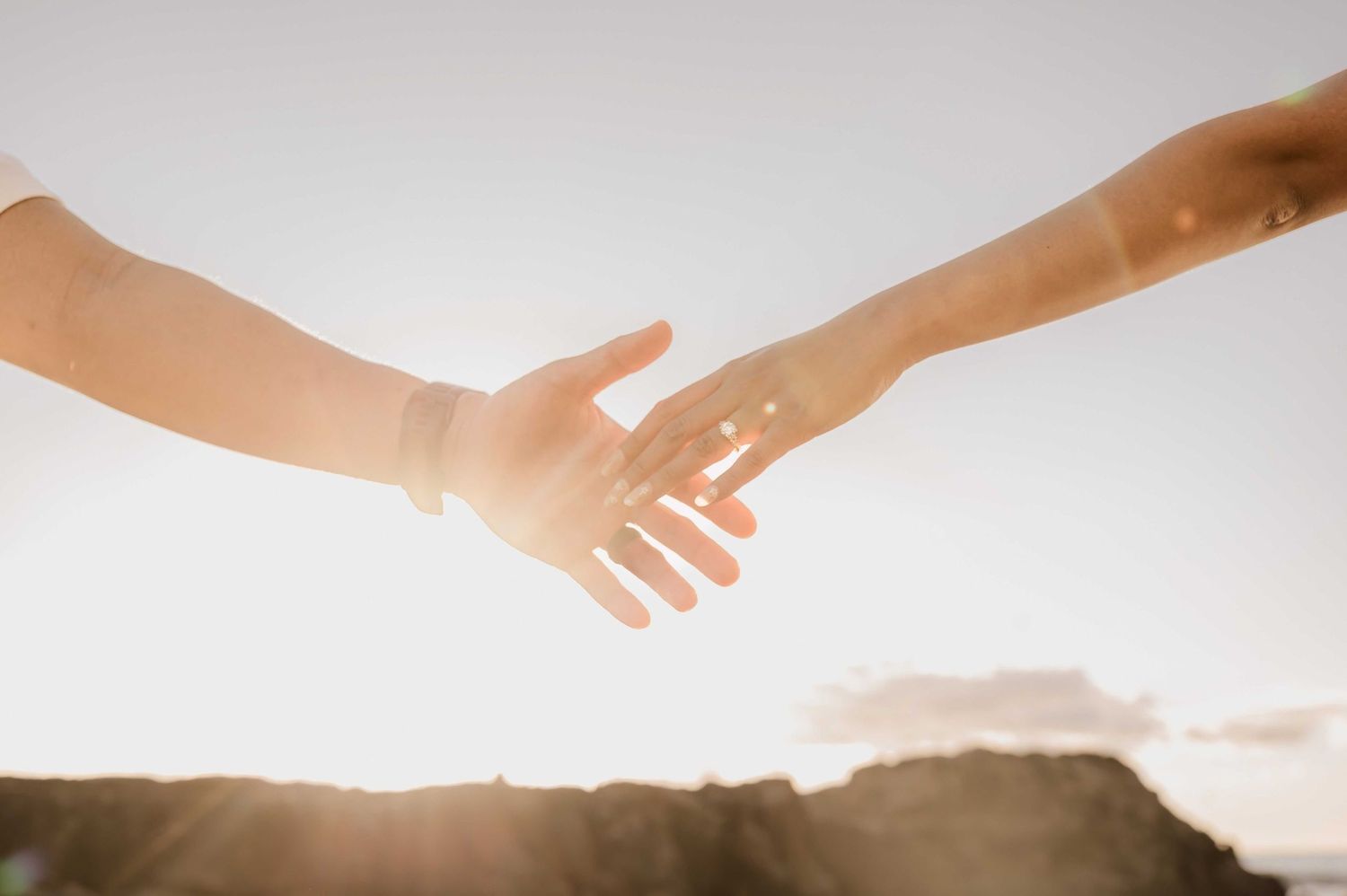 Two people reaching out to hold hands against a bright sunlit sky, symbolizing connection and support.