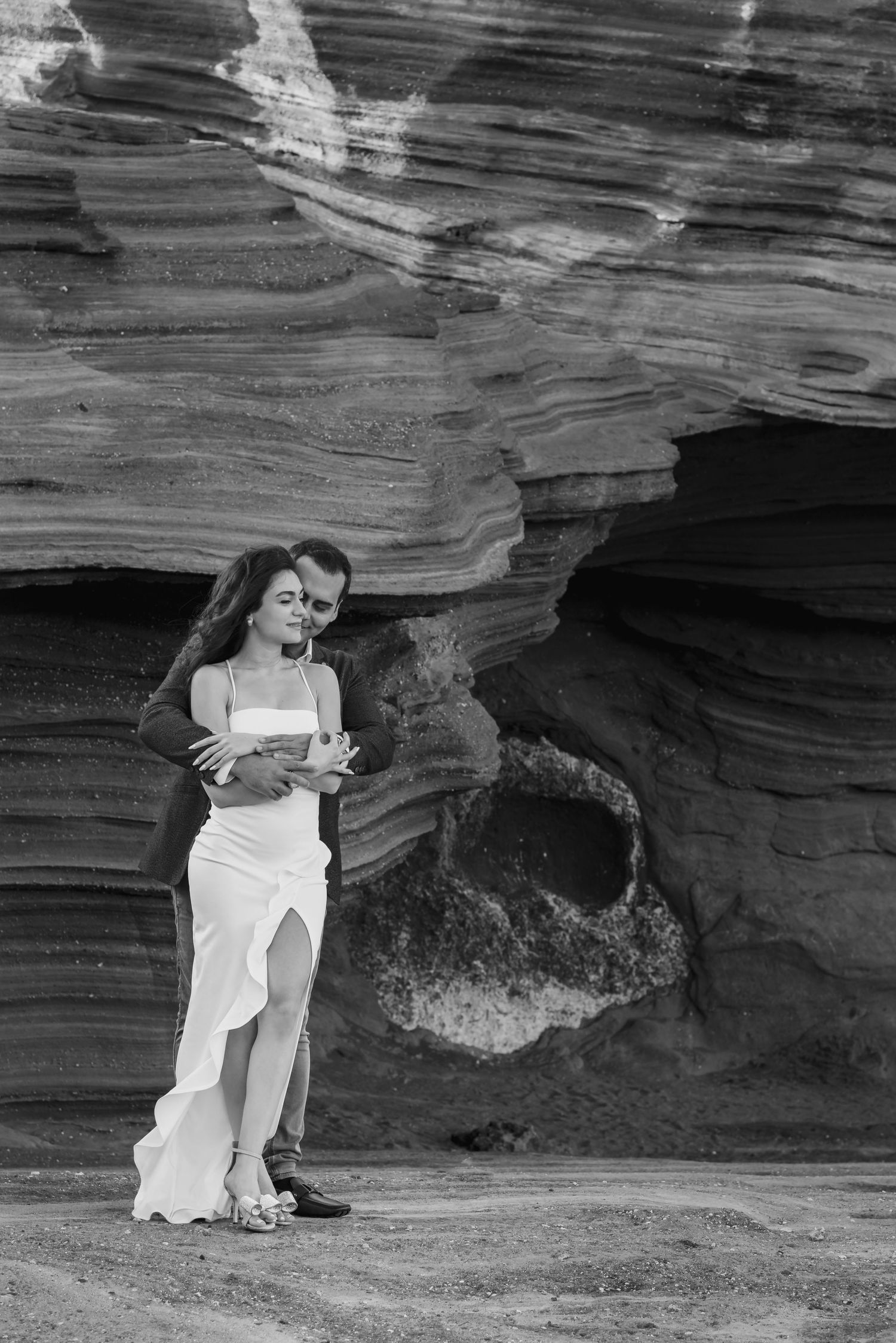 A person in a white dress sits against a dramatic rocky cliff face in black and white photography.