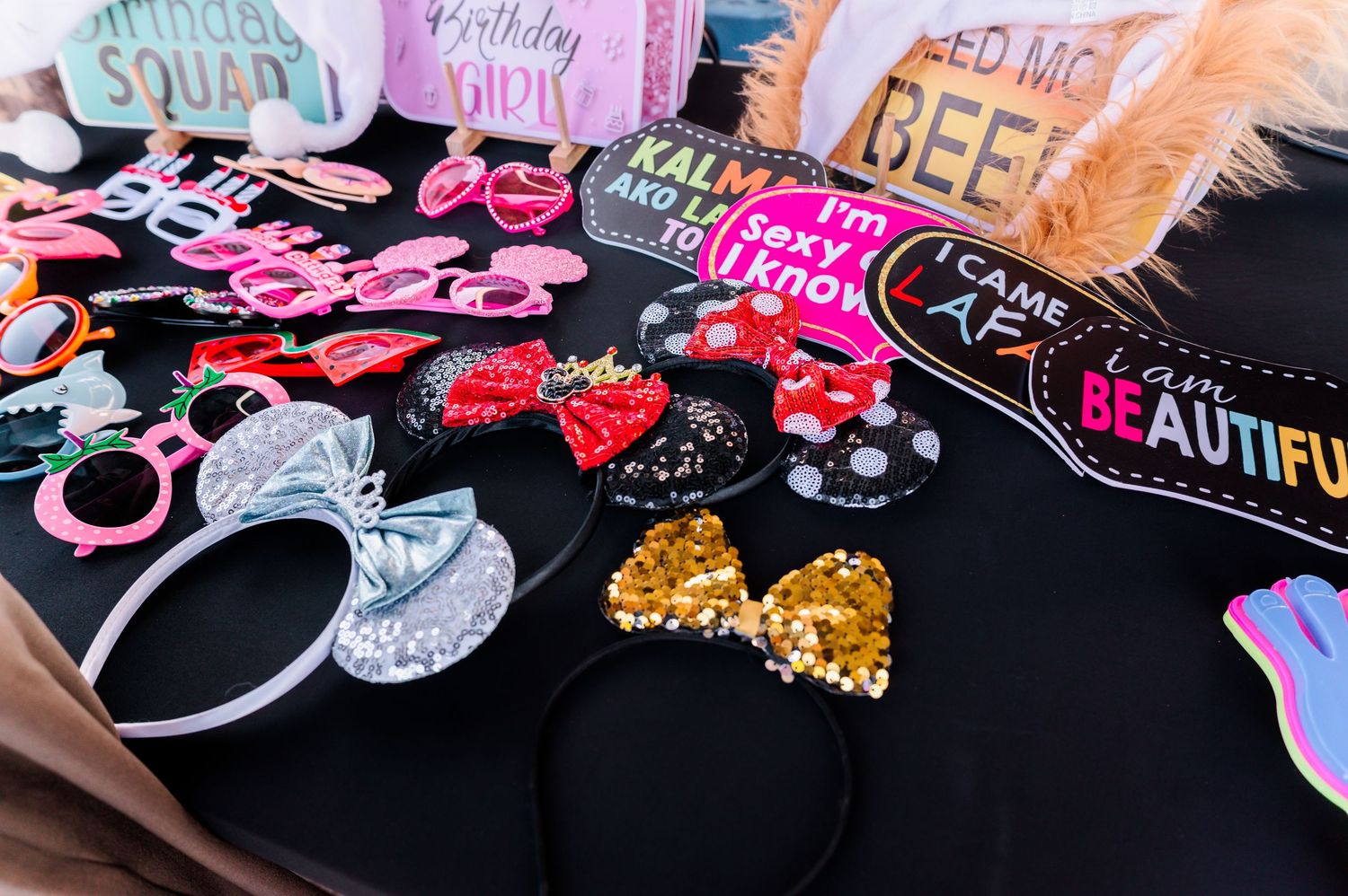 Colorful birthday party photo booth props including headbands, glasses, and signs on a black table.