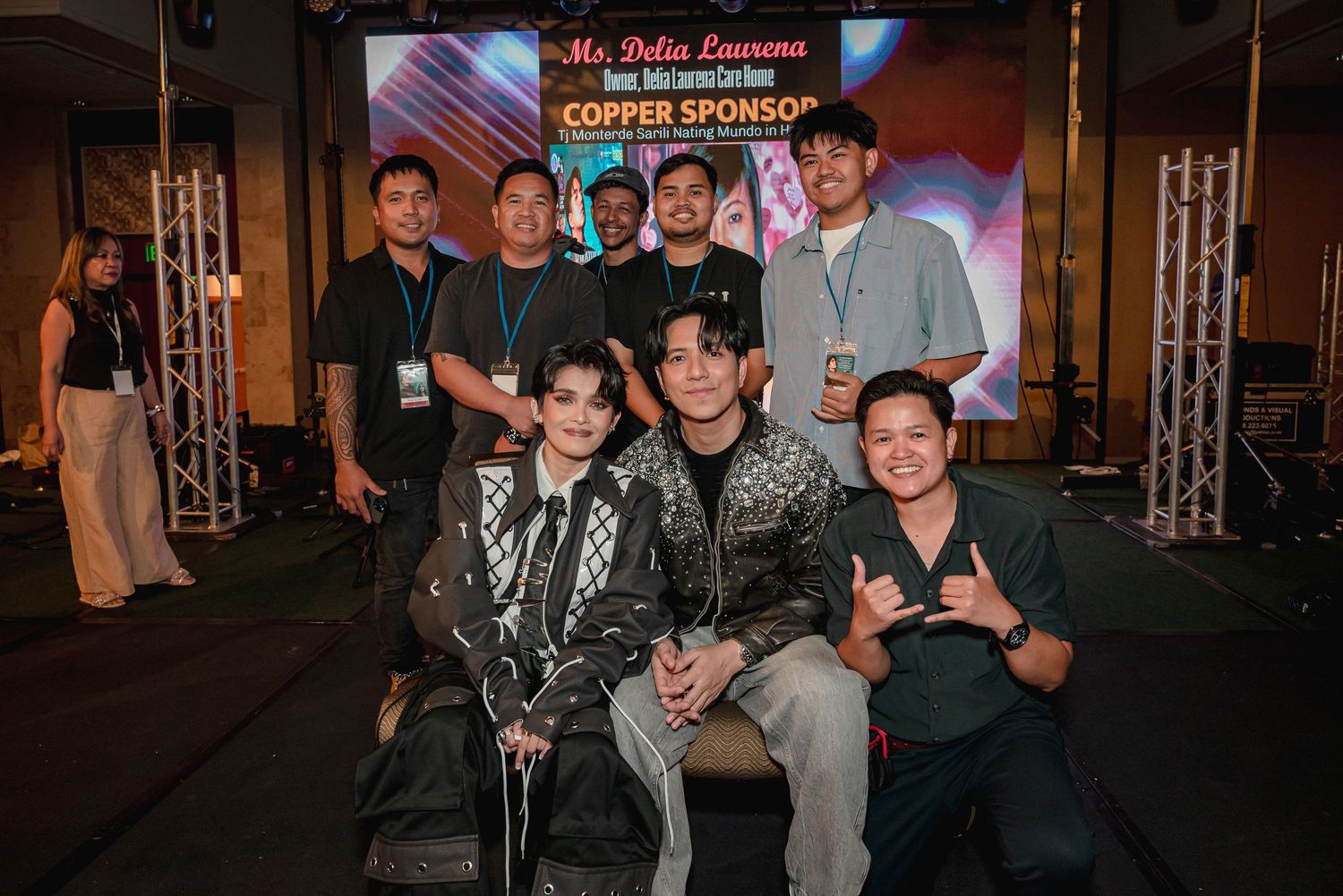 Group of people posing together at a copper sponsor event with a colorful backdrop and stage lighting.