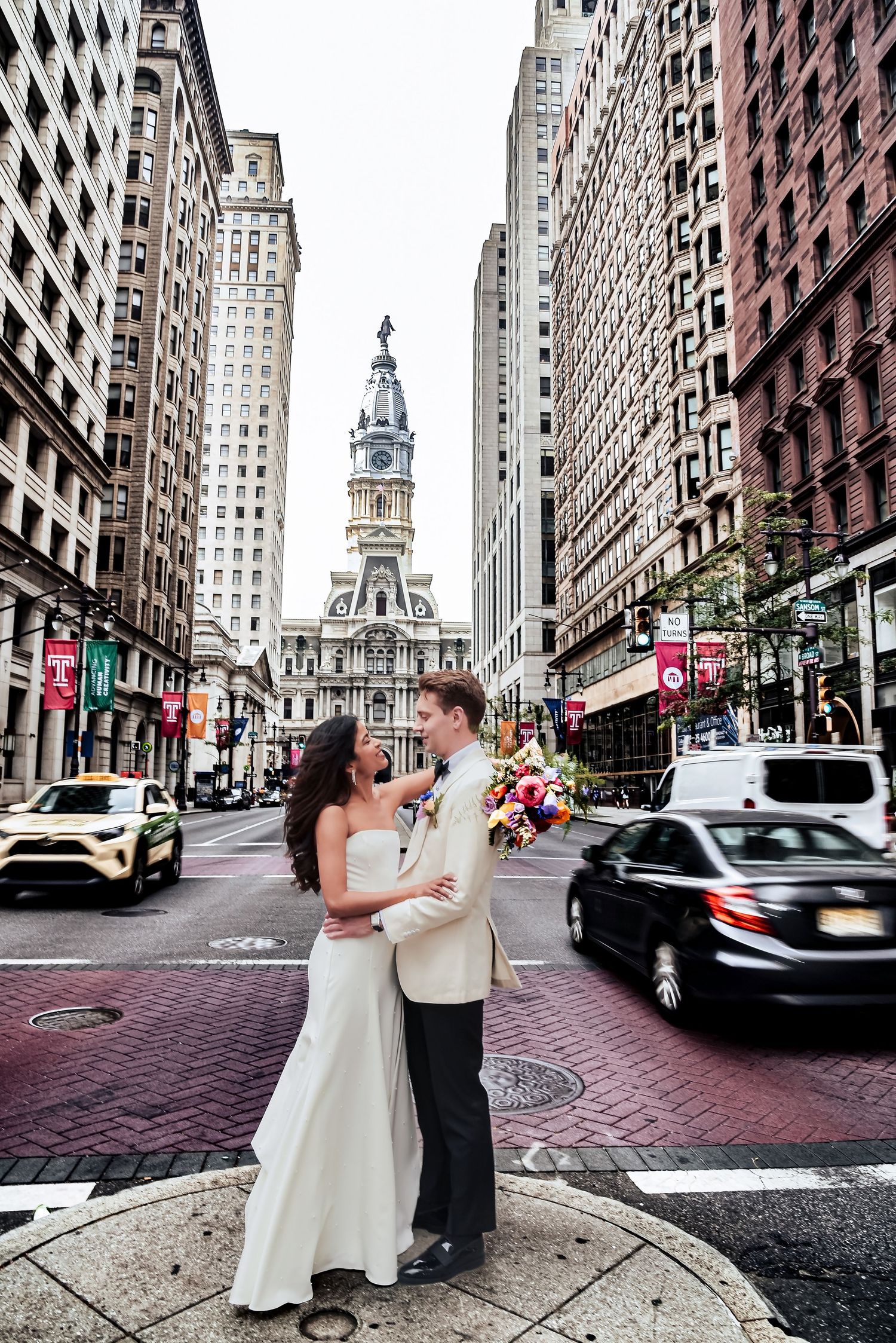 A romantic couple embraces on a brick-paved street in Philadelphia's historic district with City Hall tower in the background.