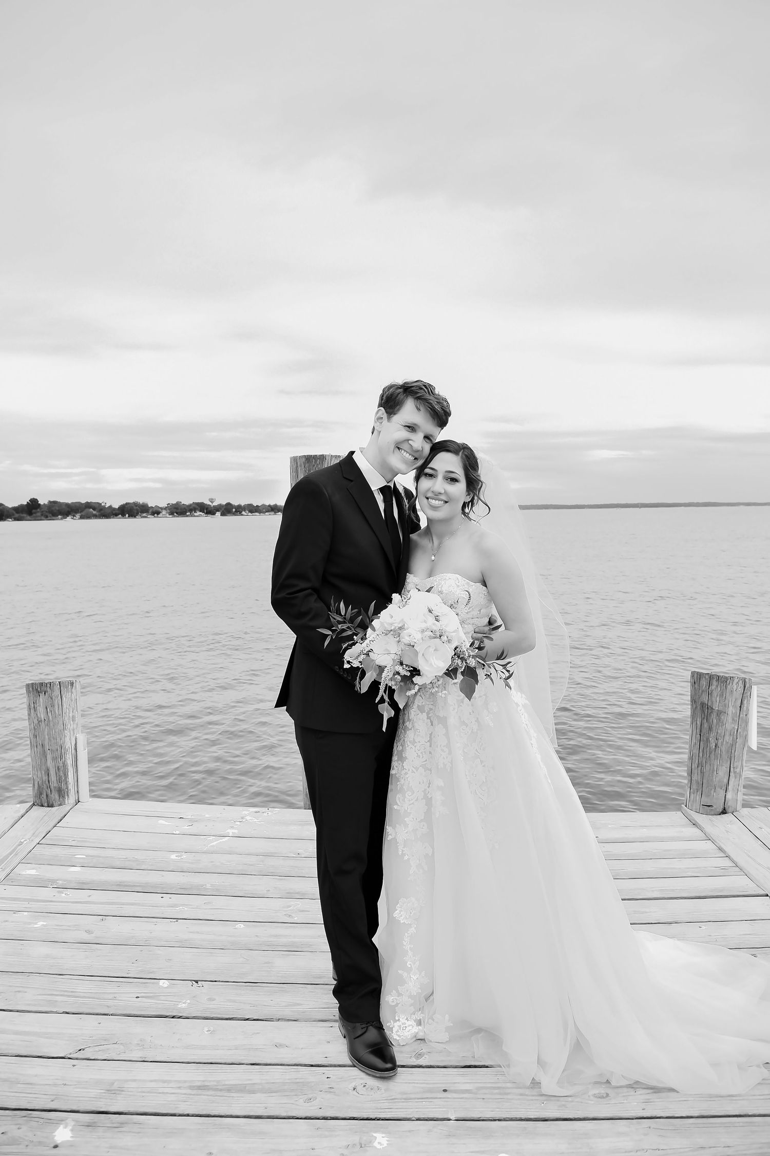 A couple in wedding attire shares romantic moments on a wooden dock by a serene waterfront.