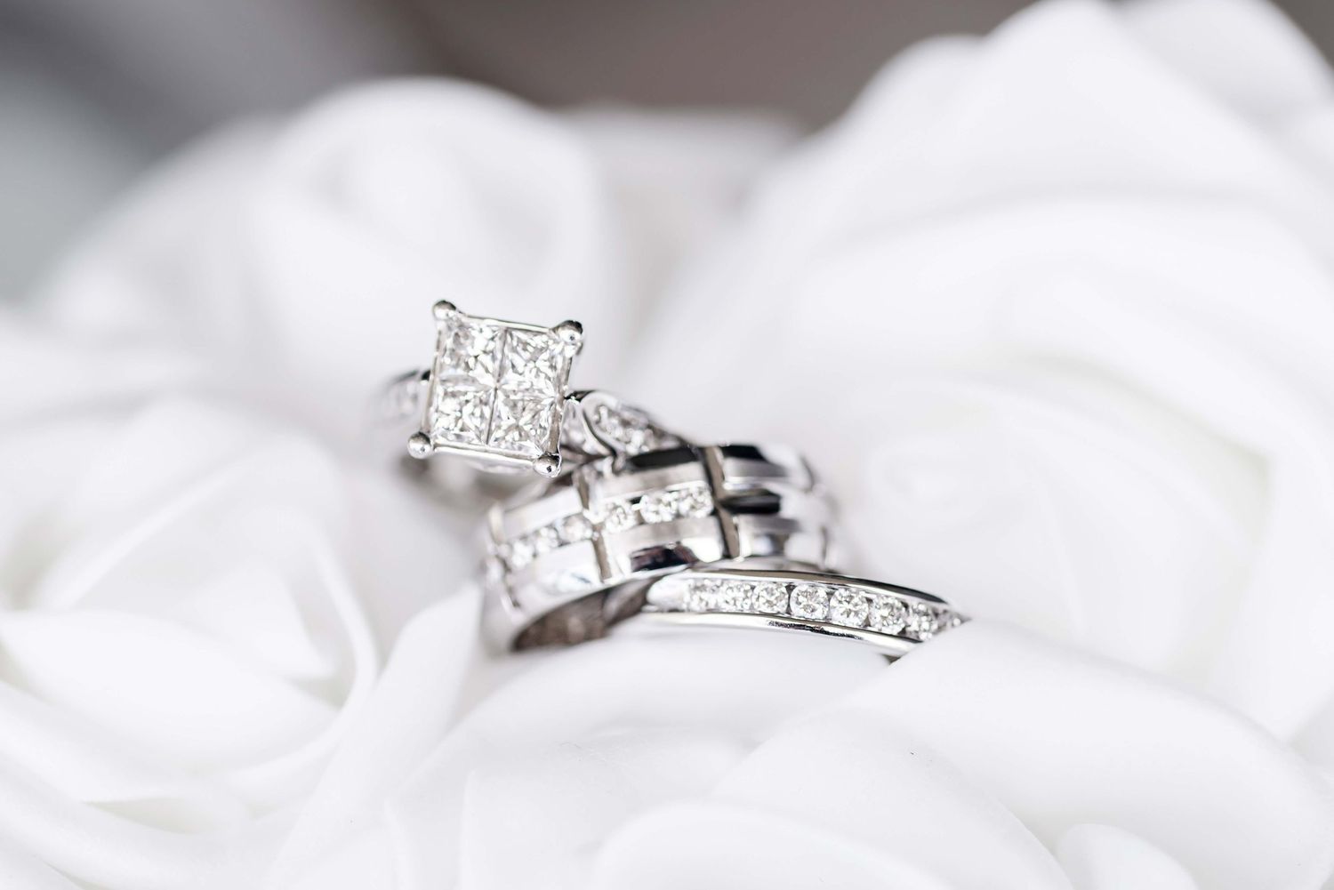 Elegant white gold engagement ring with a brilliant princess cut diamond displayed on soft white fabric.