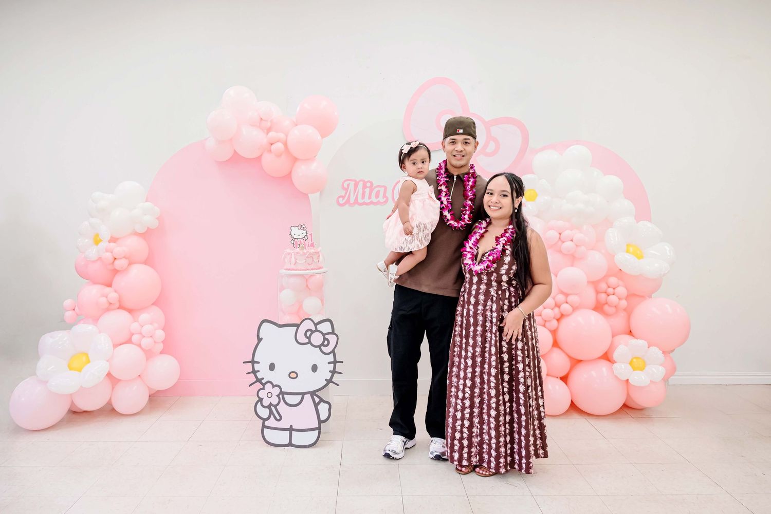 Family posing at a Hello Kitty themed birthday party with pink balloon arch and floral decorations.