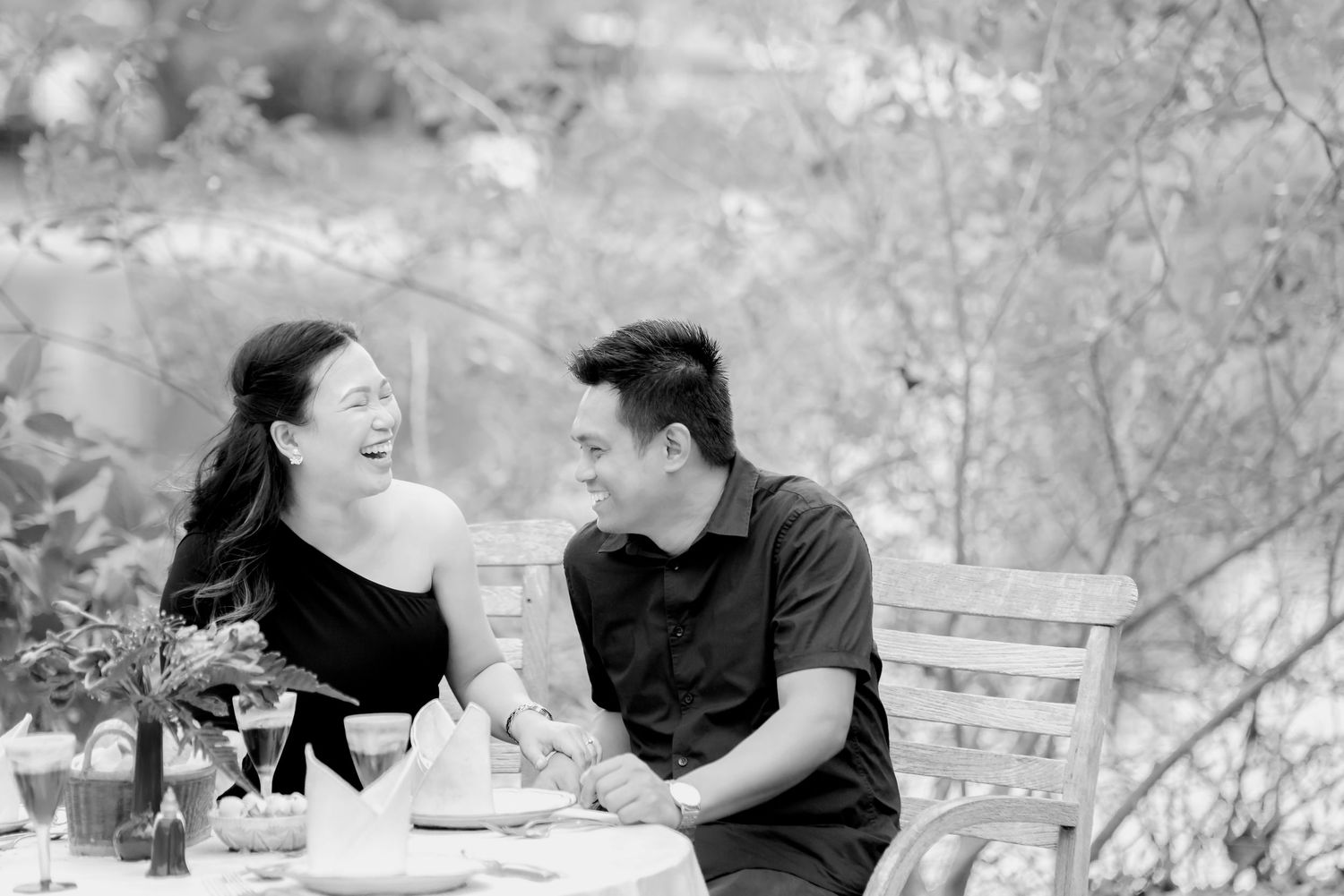 Black and white photo series showing a couple laughing and embracing outdoors in a natural setting.