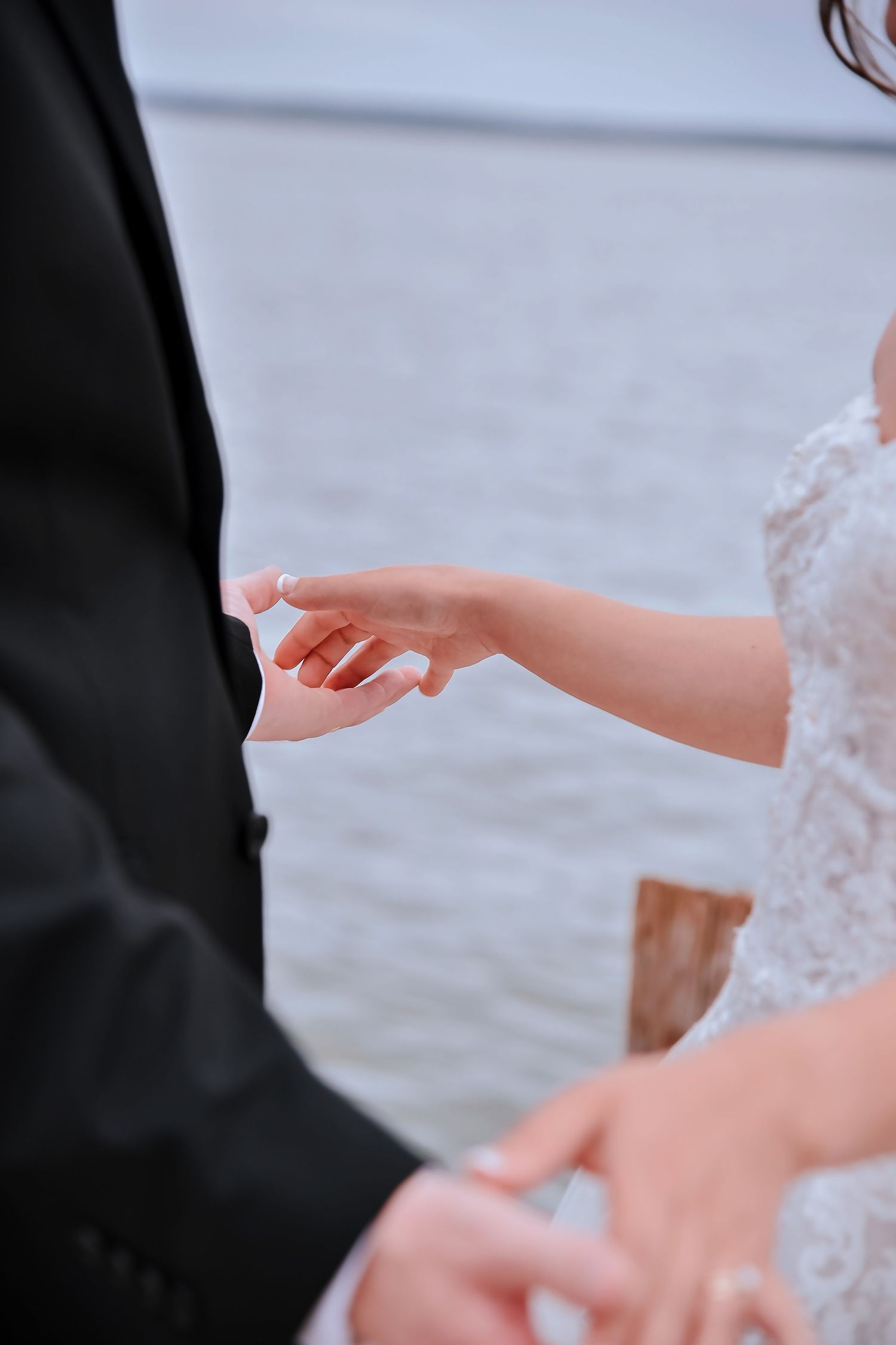 Close-up view of hands exchanging rings during an outdoor wedding ceremony by the water.