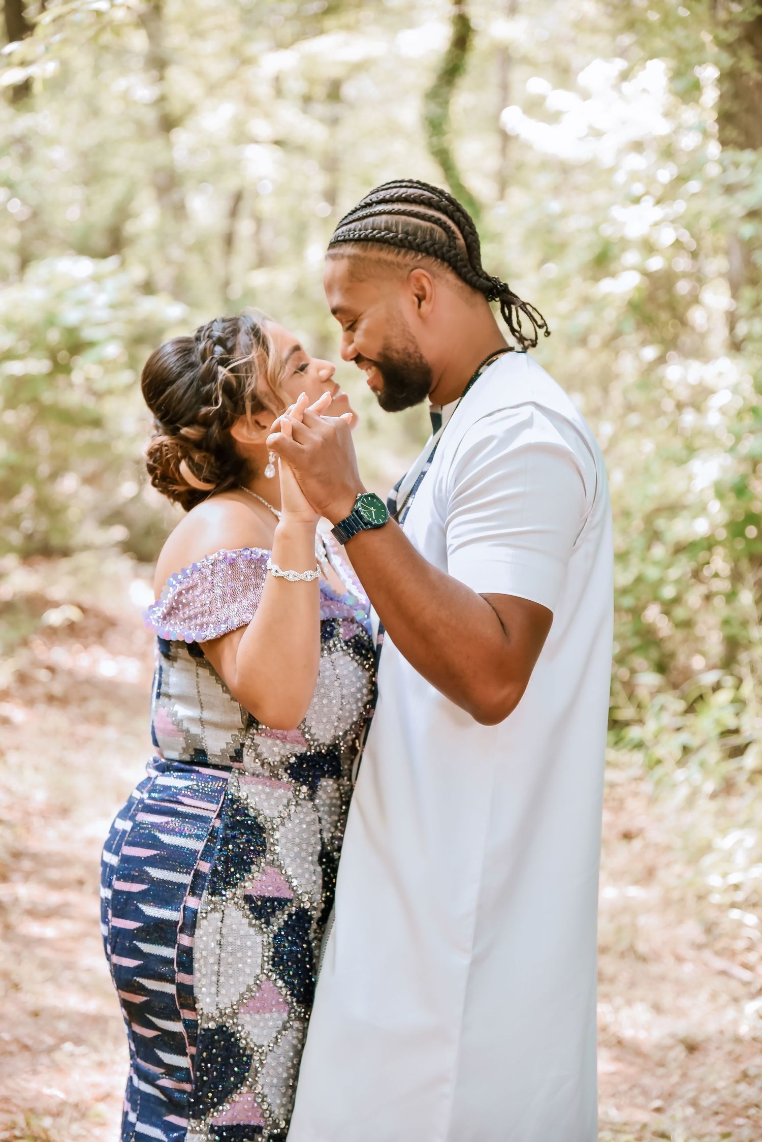 A couple shares a romantic moment in a sunlit forest, the man gently holding the woman's hand near his lips.