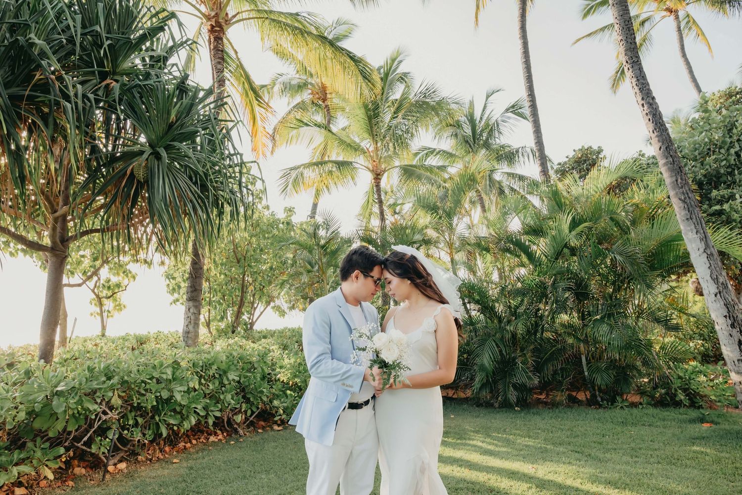Couple embracing among tropical palm trees in a lush garden setting during golden hour.