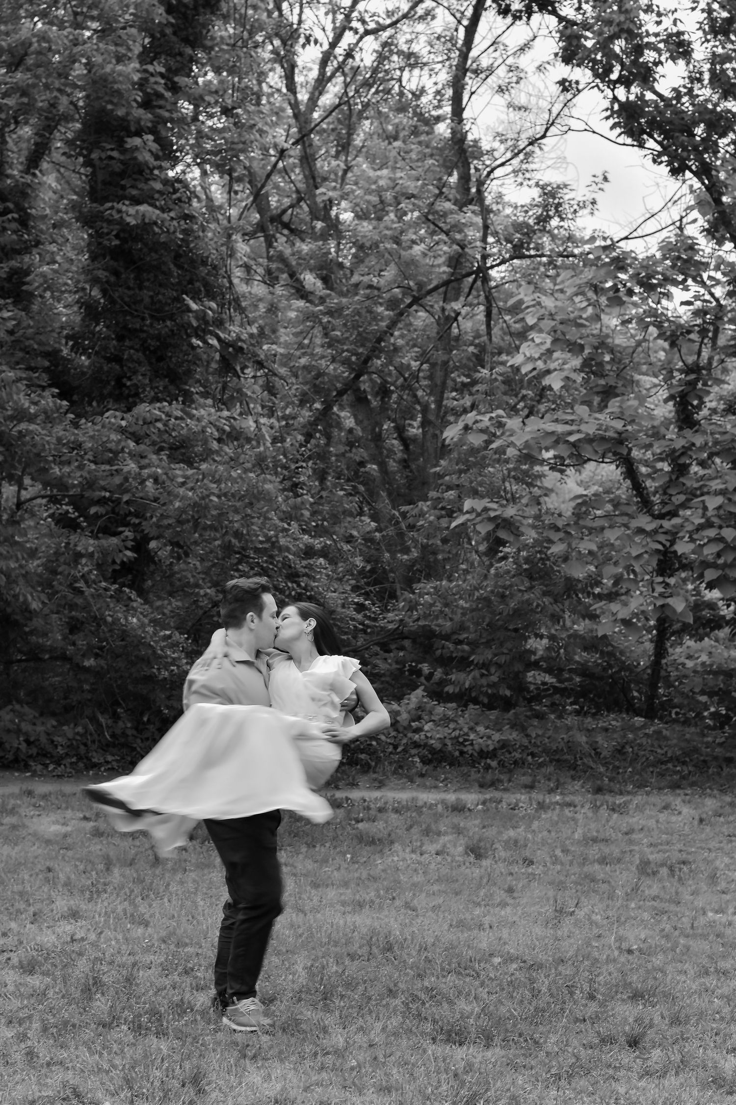 A romantic black and white photograph shows a couple embracing in a tender dance pose against a wooded backdrop.
