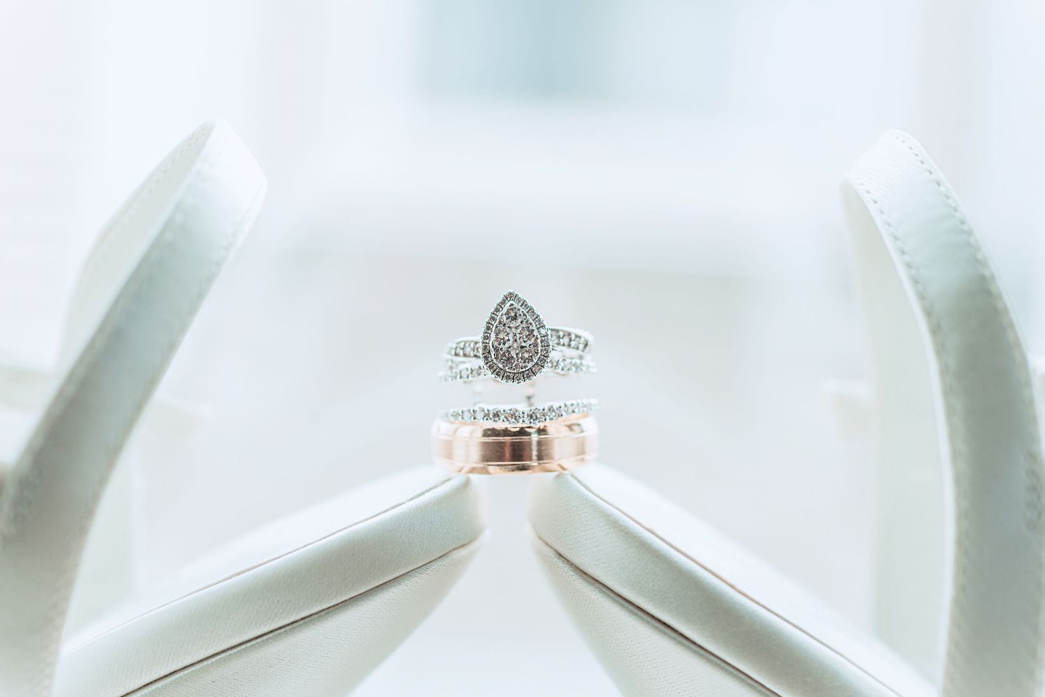 An elegant halo engagement ring with a round center diamond sits on a reflective white surface in soft lighting.