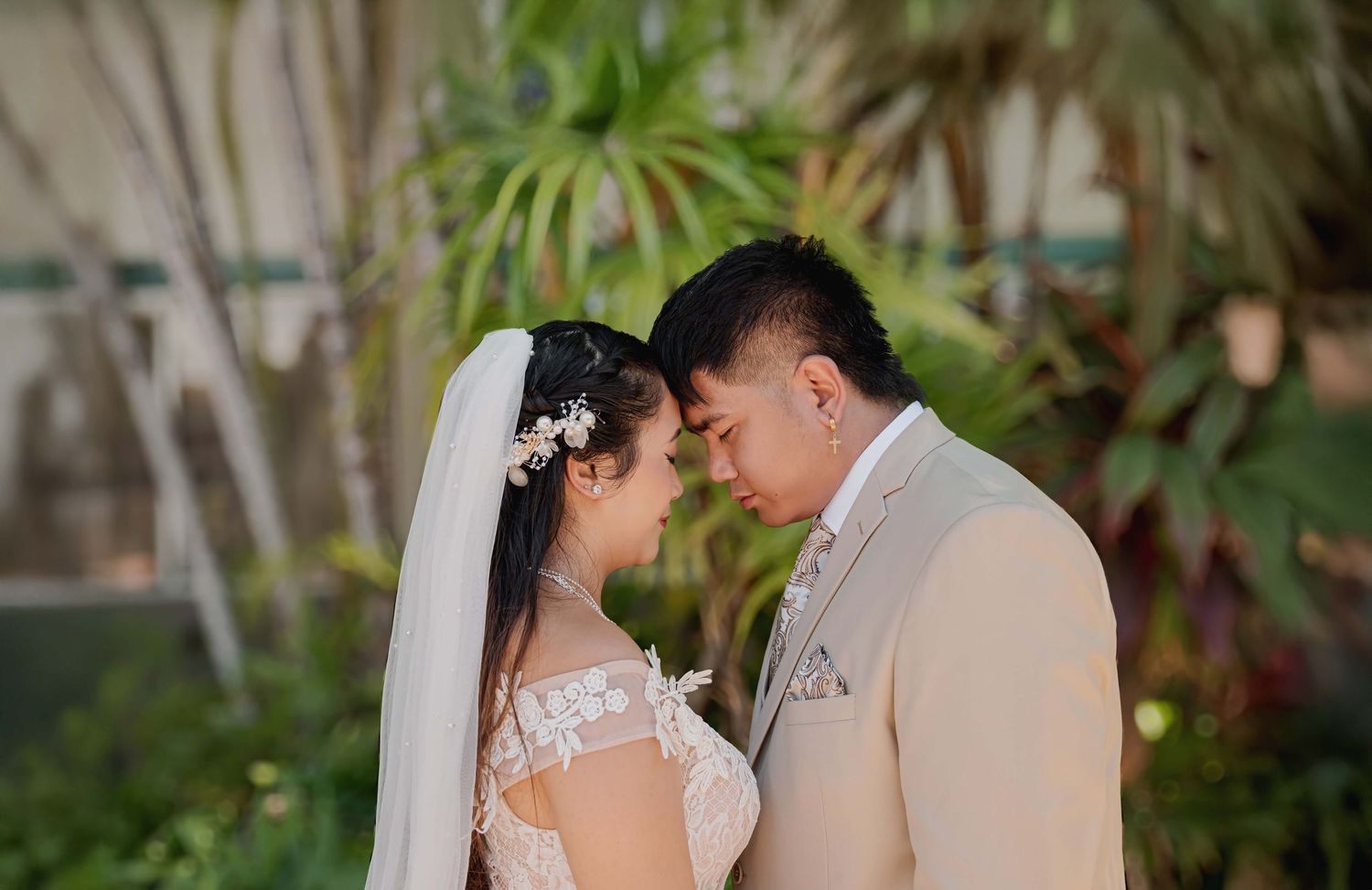 Romantic wedding couple share an intimate moment in a tropical garden setting with soft natural lighting.