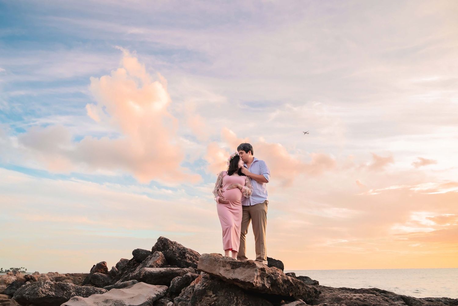 A couple stands silhouetted against a colorful sunset sky on a rocky mountain overlook during golden hour.