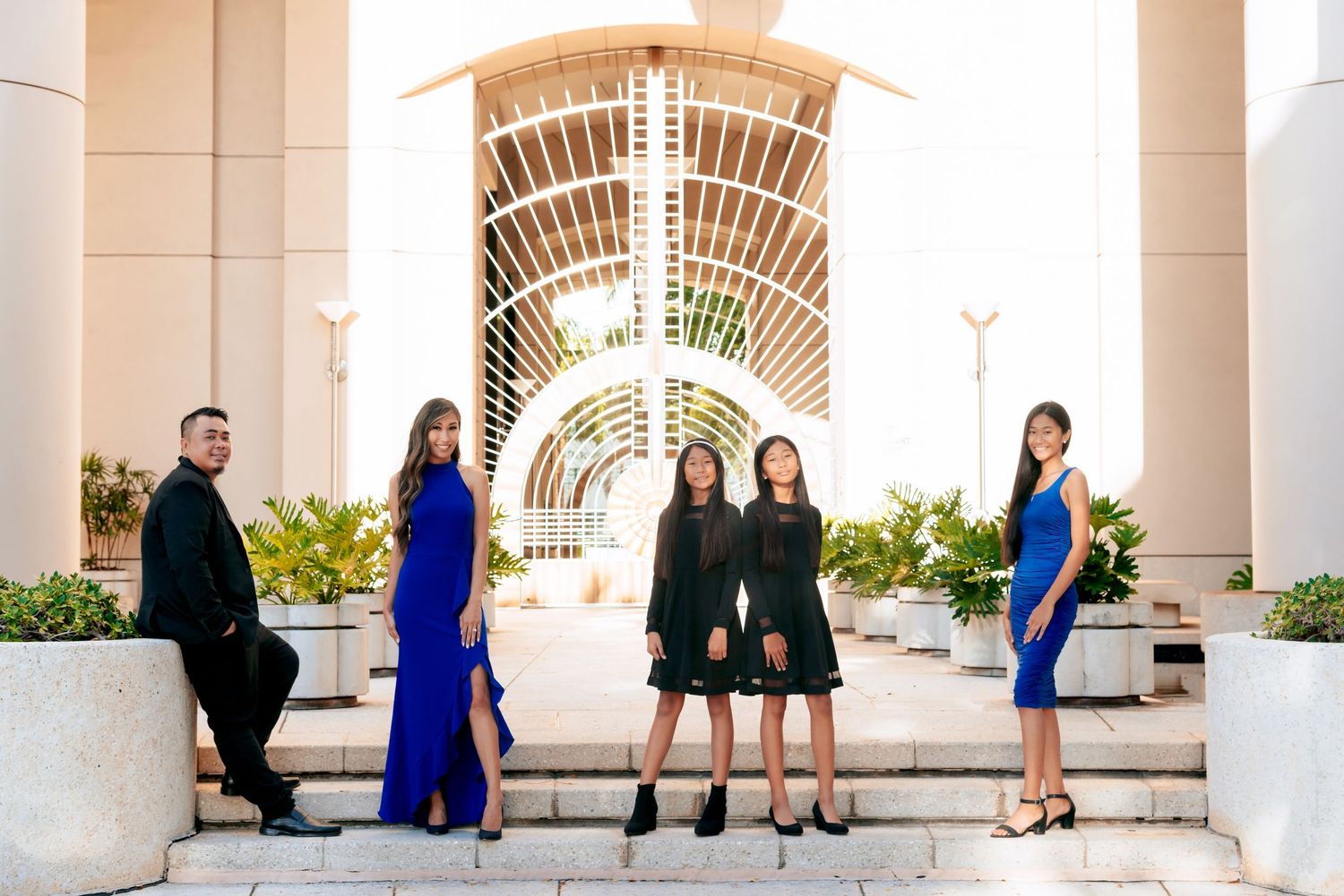 Five elegantly dressed people posing on steps outside a modern building with arched architecture.