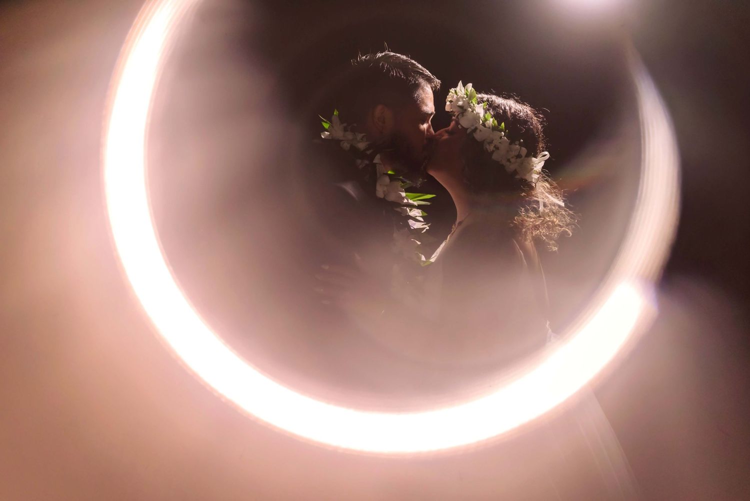 Couple sharing a romantic kiss framed by a glowing circular light ring at a wedding ceremony.