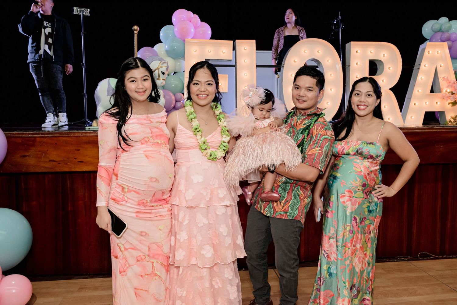 Group of five people posing together at a Flora-themed celebration with colorful balloons and decorations.
