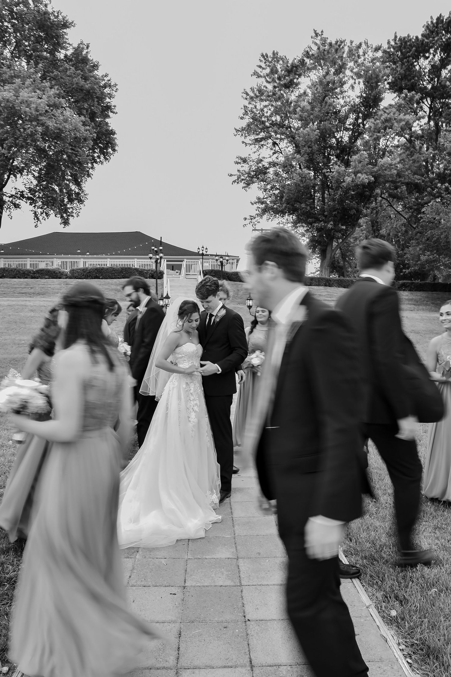 A series of black and white wedding photos showing couples walking and dancing at an outdoor reception venue.