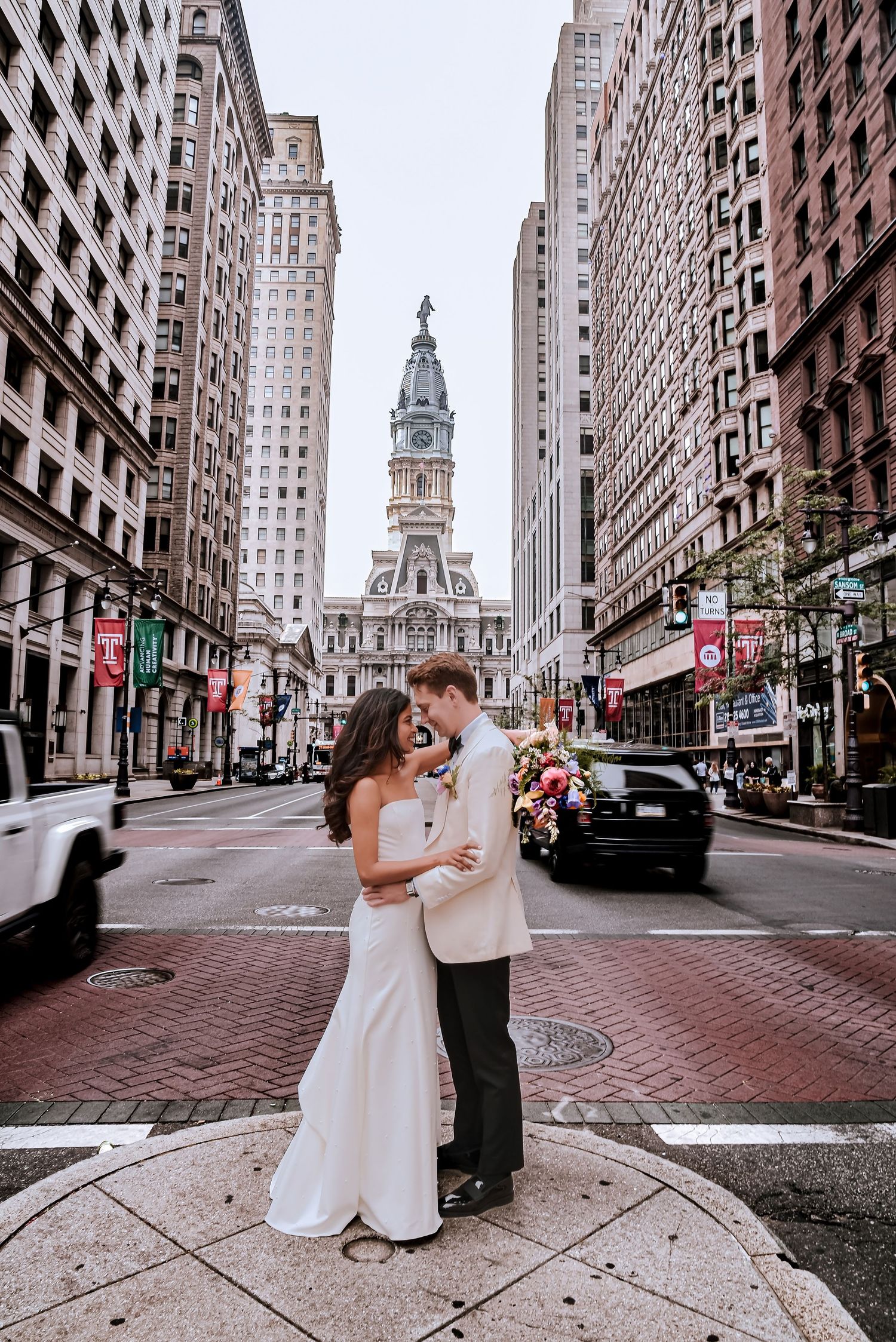 Bride and groom embrace on Philadelphia street with City Hall clock tower backdrop on their wedding day.