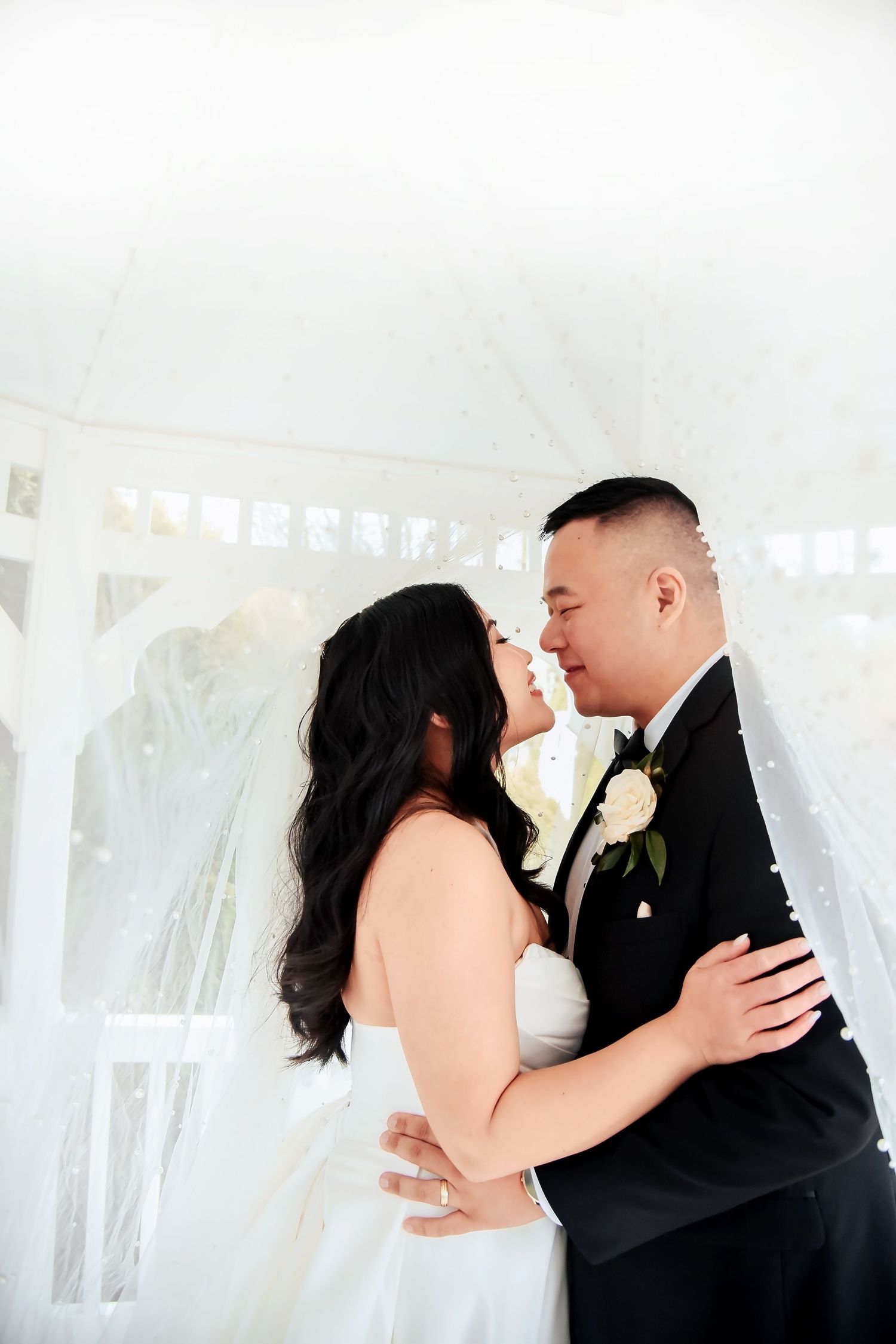 A romantic wedding moment captured under a white veil and gazebo as a couple shares their first kiss.